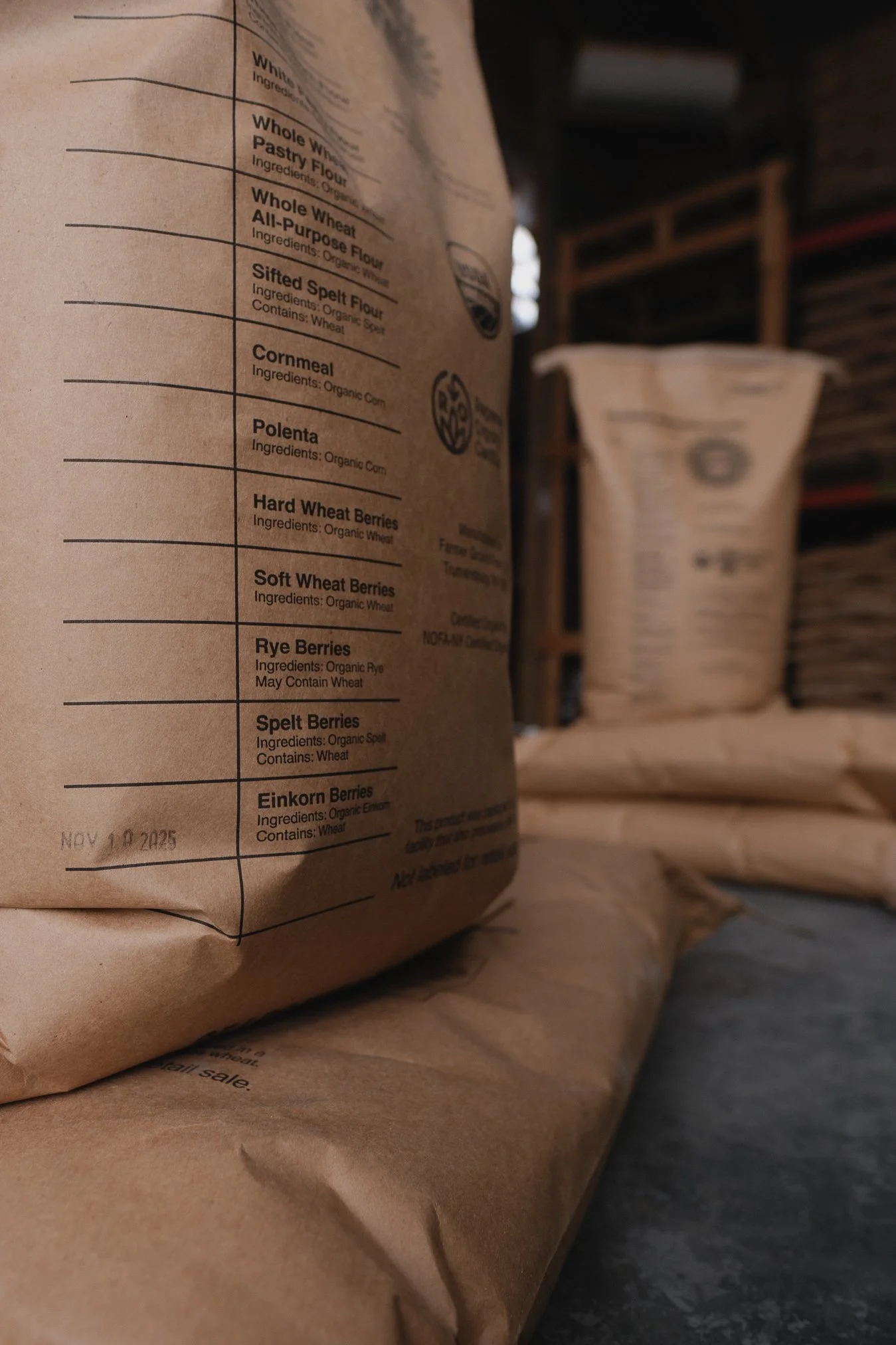 Close-up of brown paper bags with organic flour and berry ingredients on a shelf, with another bag in the background.