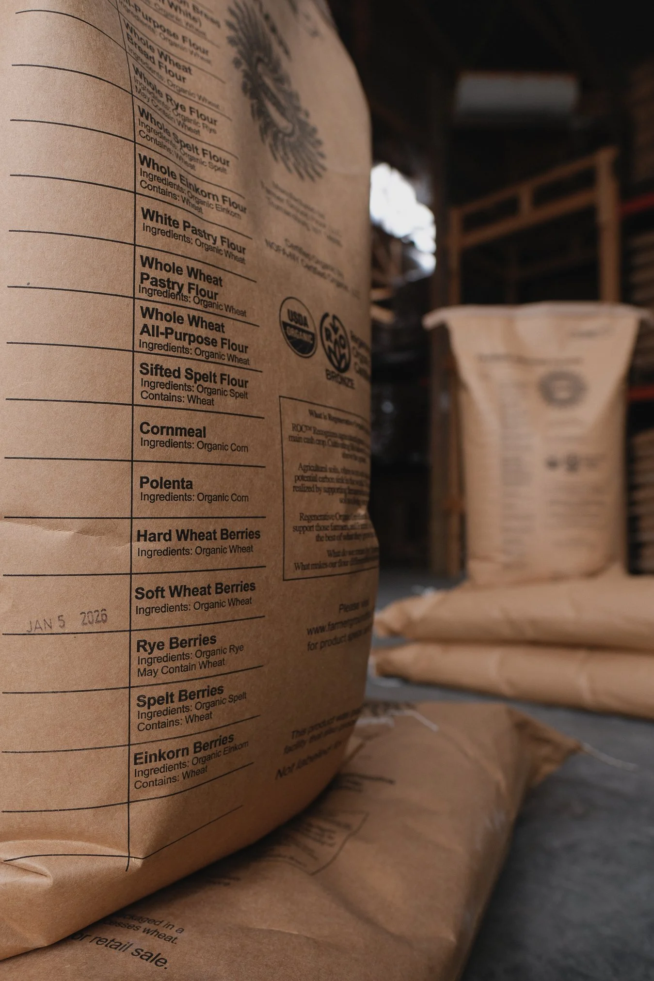 Bags of organic flours and berries stacked on a shelf in a rustic storage area.