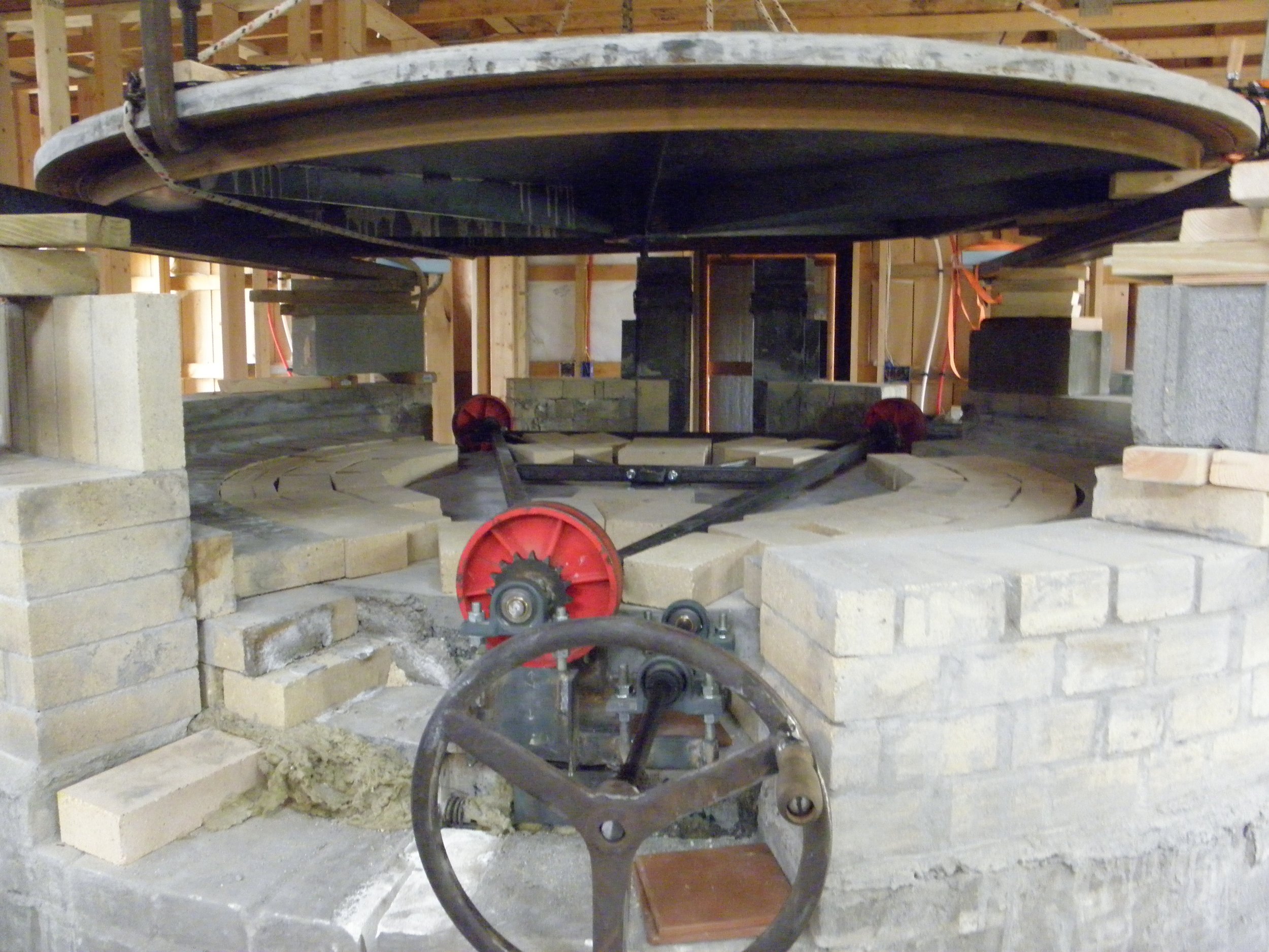 Construction of a large circular brick oven with a wooden framework seen inside a building under construction.