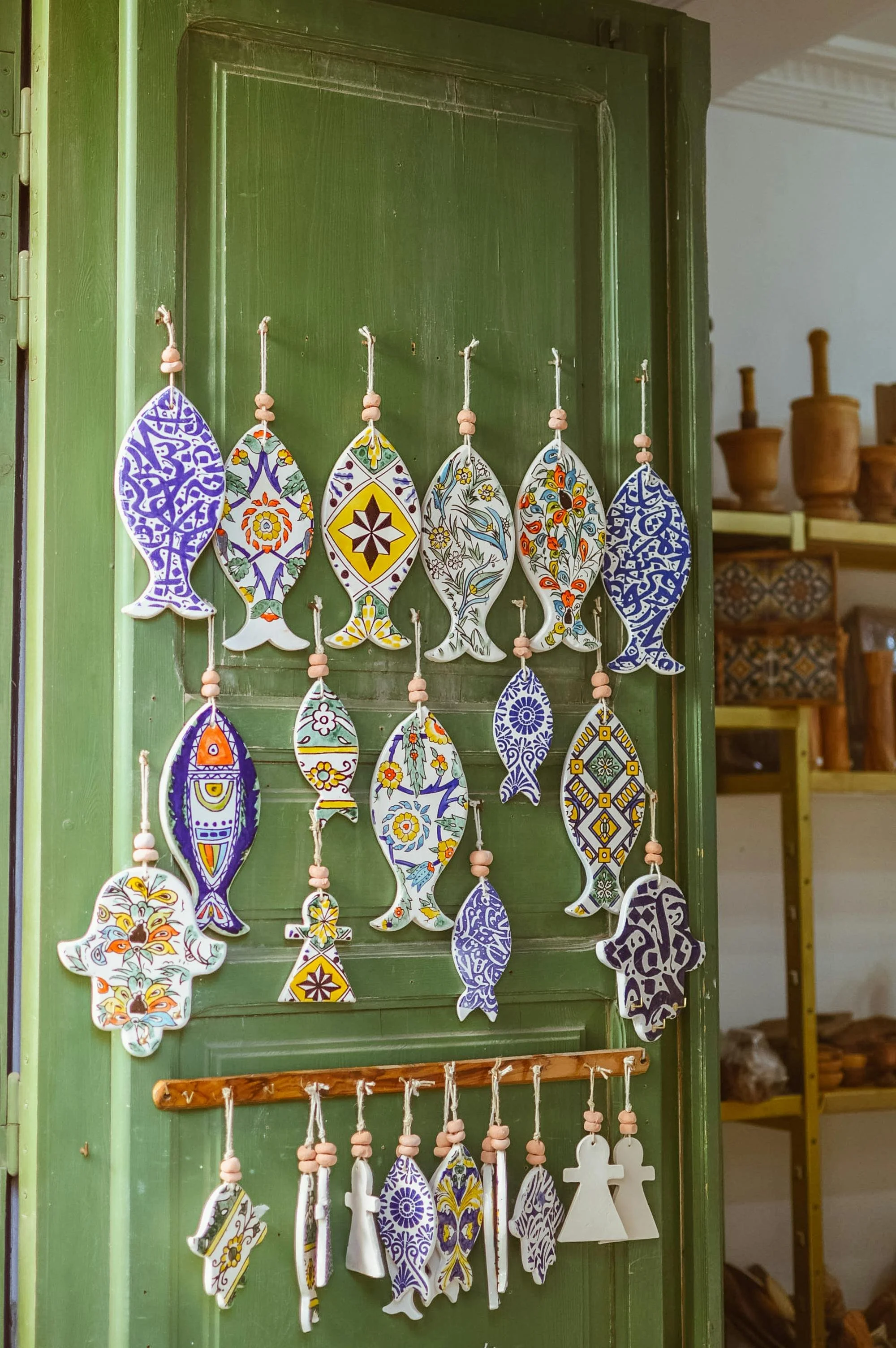 Colorful fish-shaped ceramic ornaments with floral and abstract patterns hanging on strings, displayed on a green wooden door.