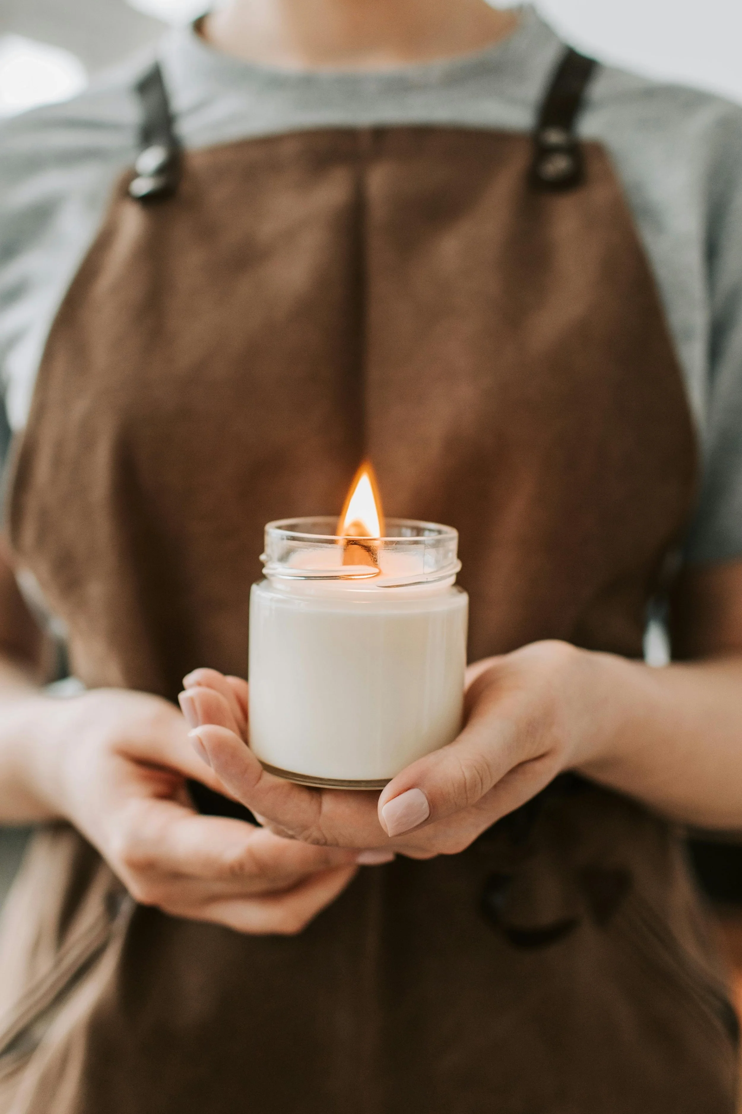 Person holding a lit candle in a glass jar.