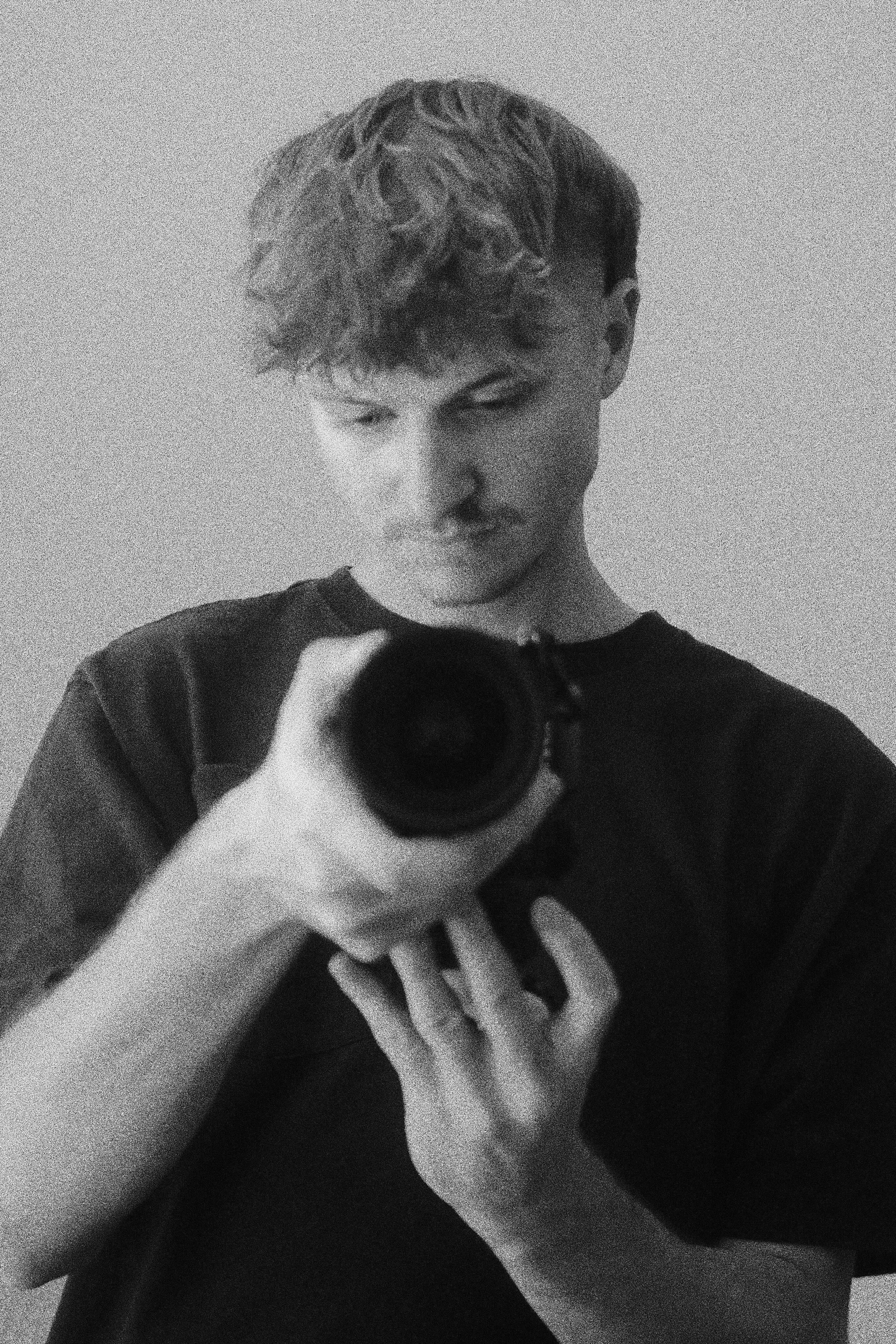 A black-and-white photo of a young person taking a selfie with a camera in front of a plain wall.