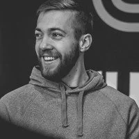 A young man with a beard smiling, wearing a hoodie.