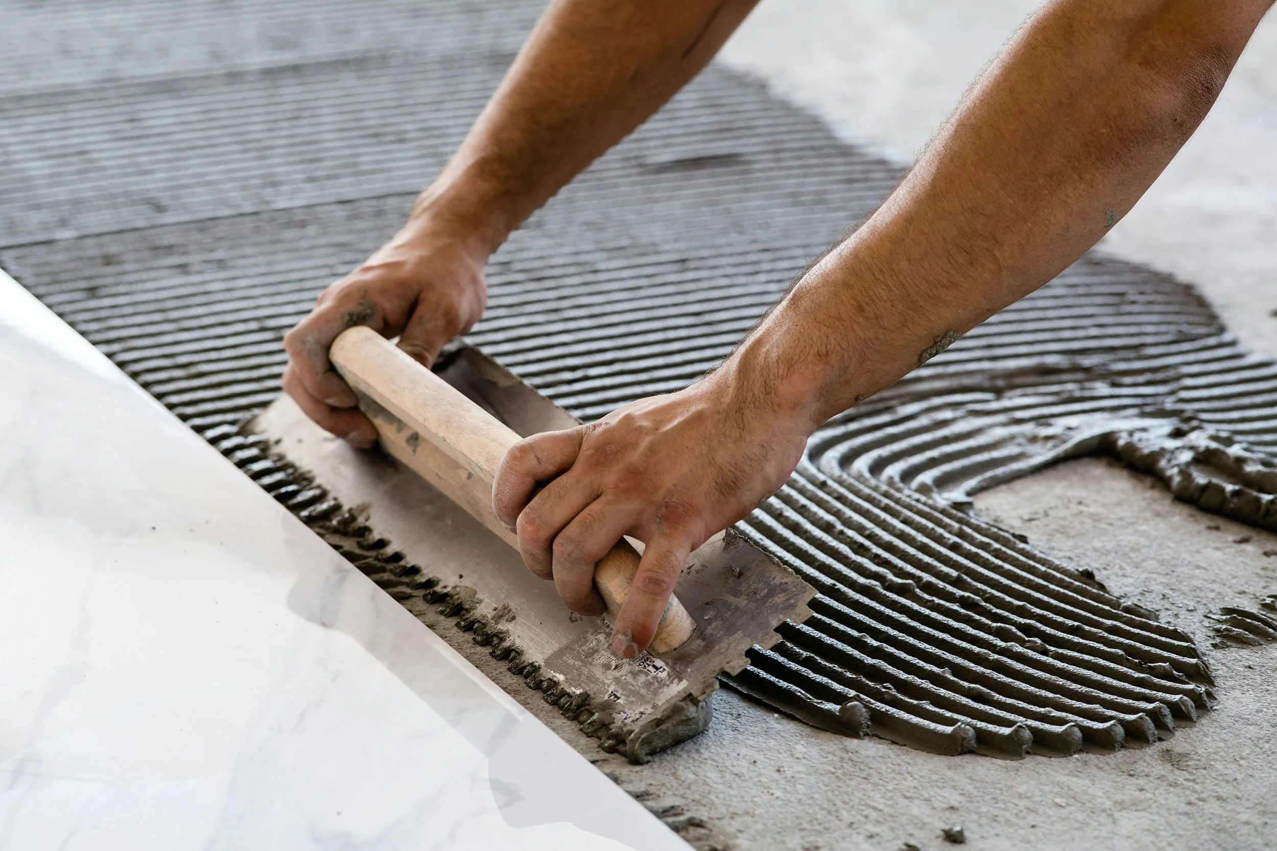 Person applying adhesive and smoothing out tiles on a floor during tiling process.