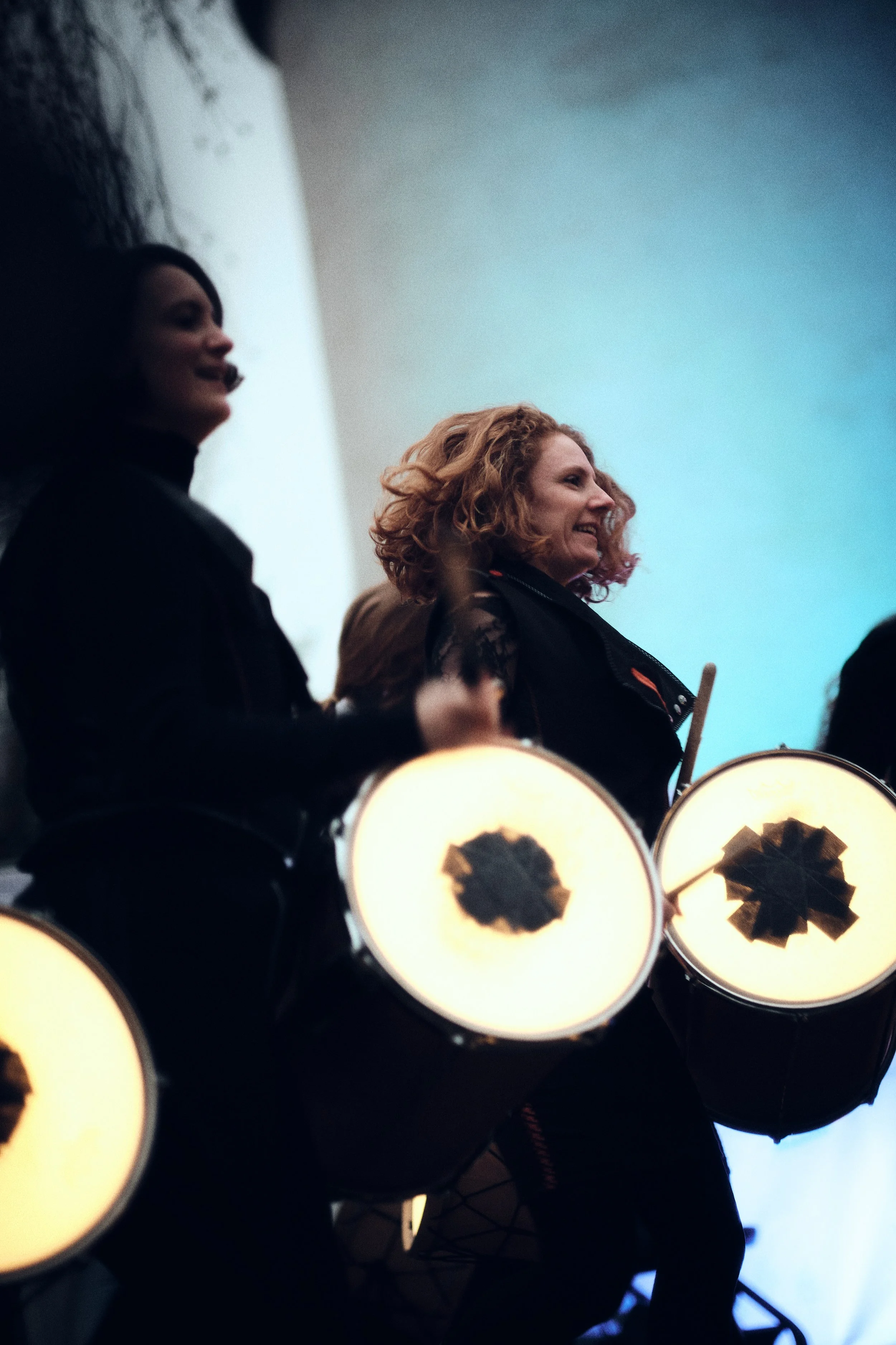 Vrouw met krullend haar die op een trommel slaat tijdens een optreden.