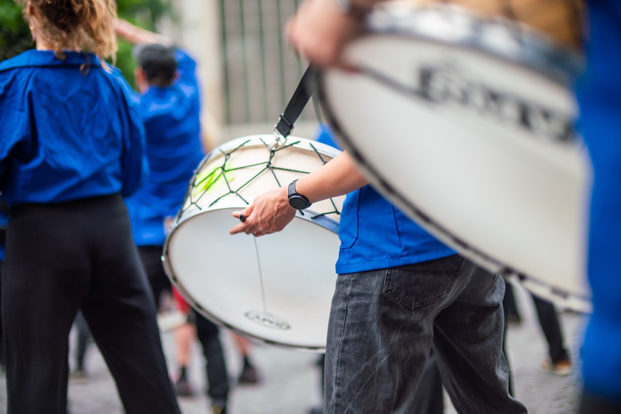 Close-up van muzikanten in blauwe hemden die op grote trommels spelen tijdens een optreden op straat.