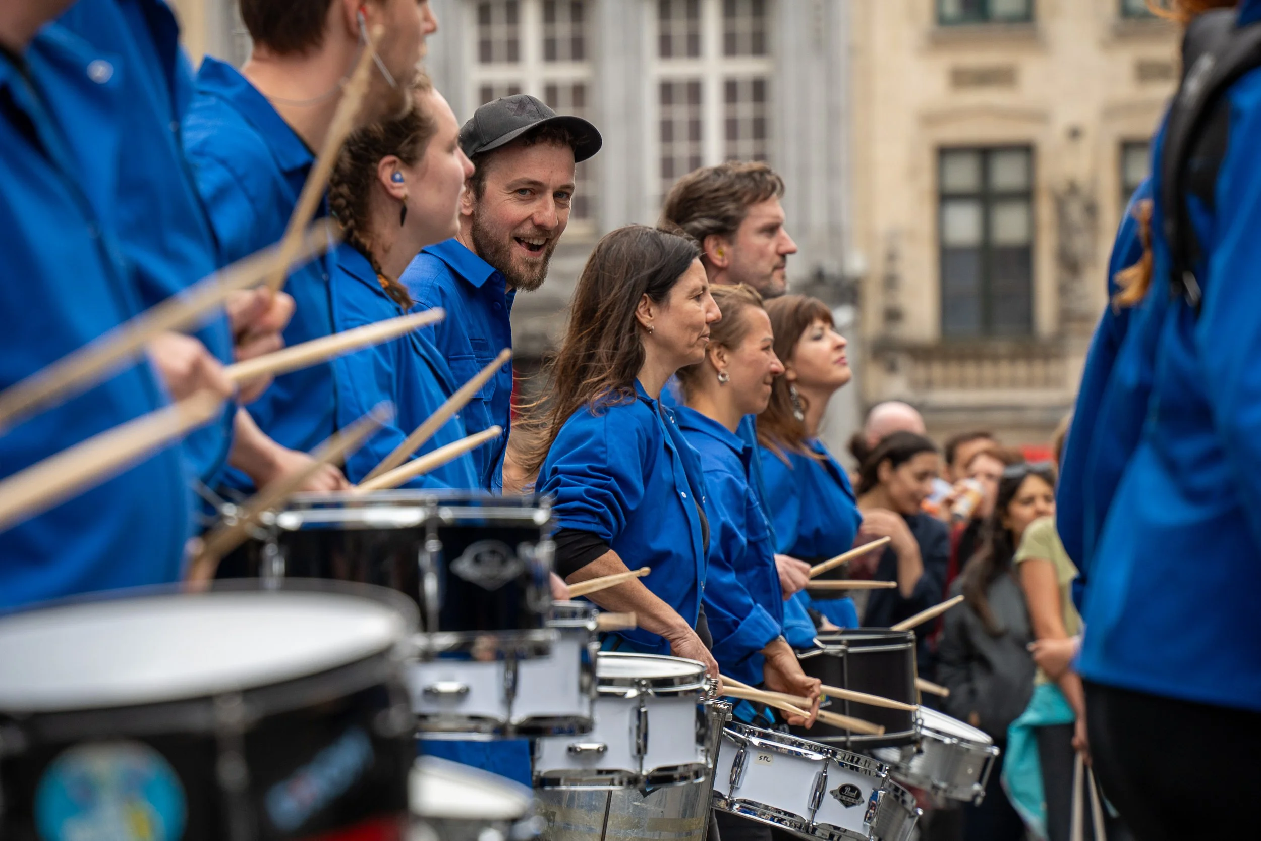 Laurens Vandevenne, mede-instructeur bij De Batterij, speelt samen met andere percussionisten in blauwe hemden tijdens een levendig straatoptreden.