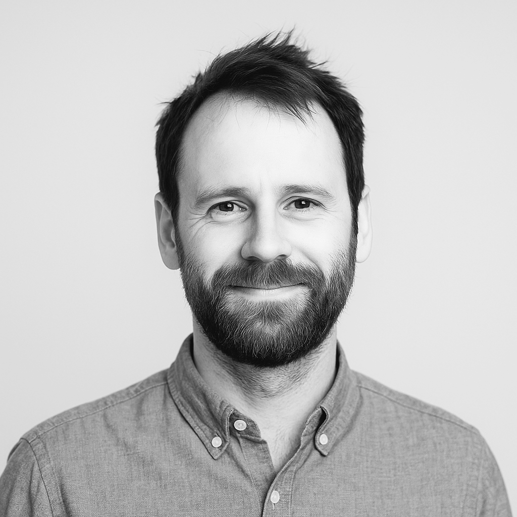 Black and white portrait of a smiling man with a beard and short hair, wearing a button-up shirt.