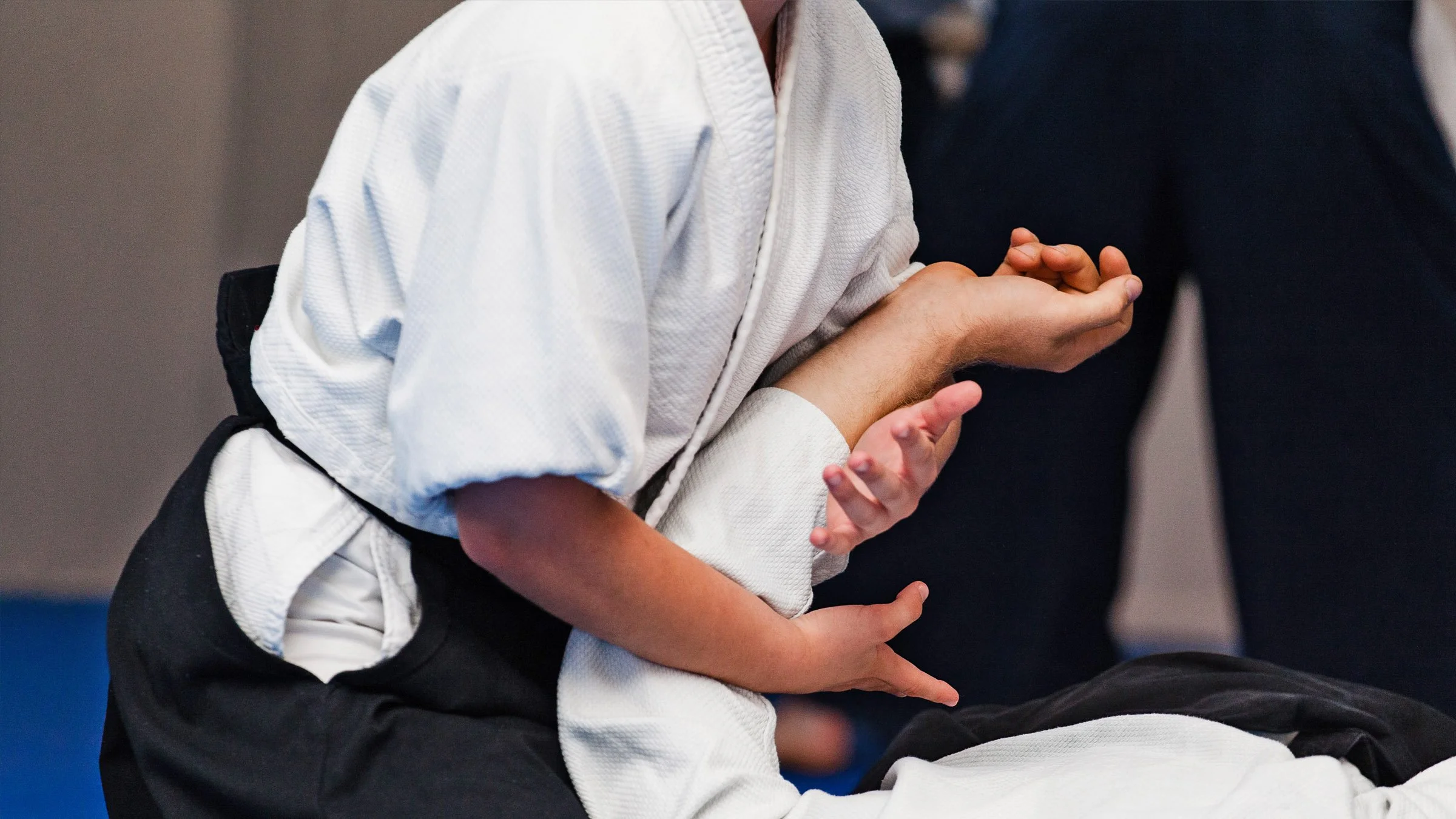 A person in a white martial arts gi demonstrating or practicing a technique with a partner at a martial arts dojo or training facility.