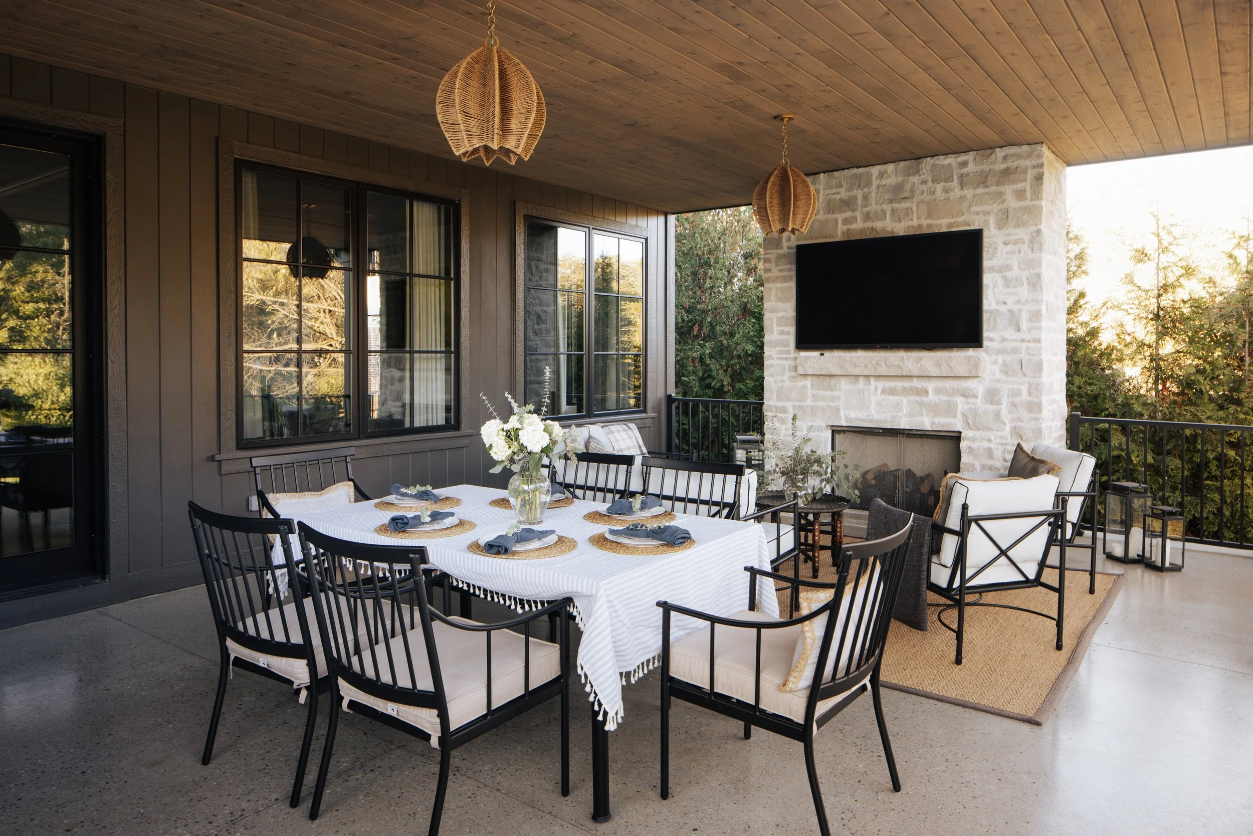 Modern lanai space with a covered outdoor dining table in front of a seating area by a modern stone-clad fireplace.