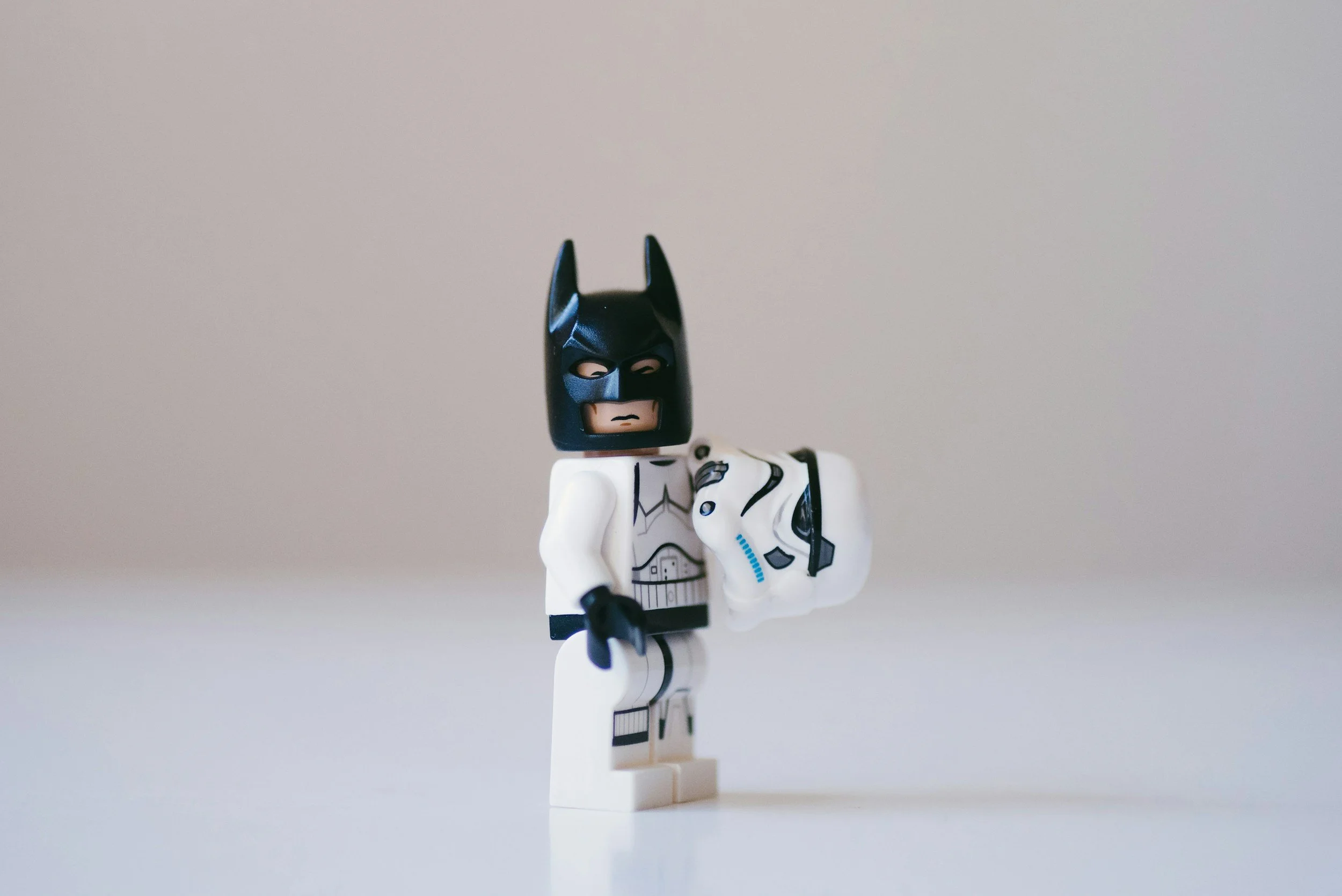 Lego Batman figure holding a stormtrooper helmet against a plain background.