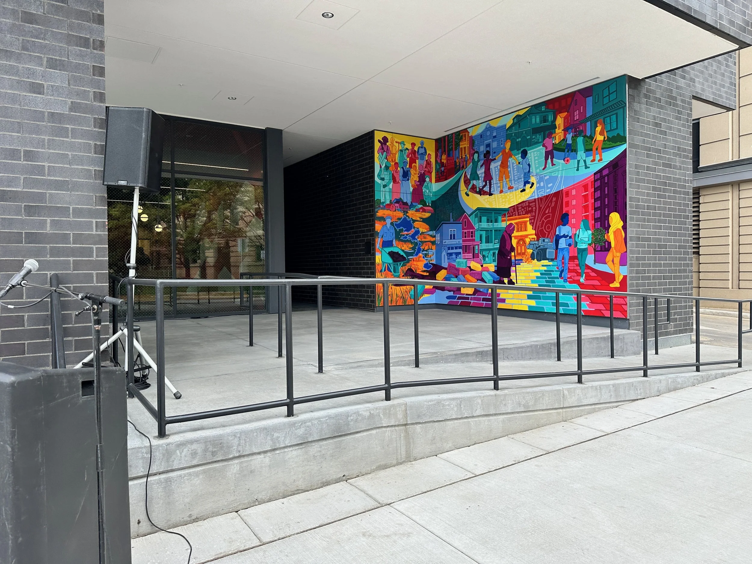 Colorful mural on building wall depicting diverse people, cityscape, and outdoor scenes.