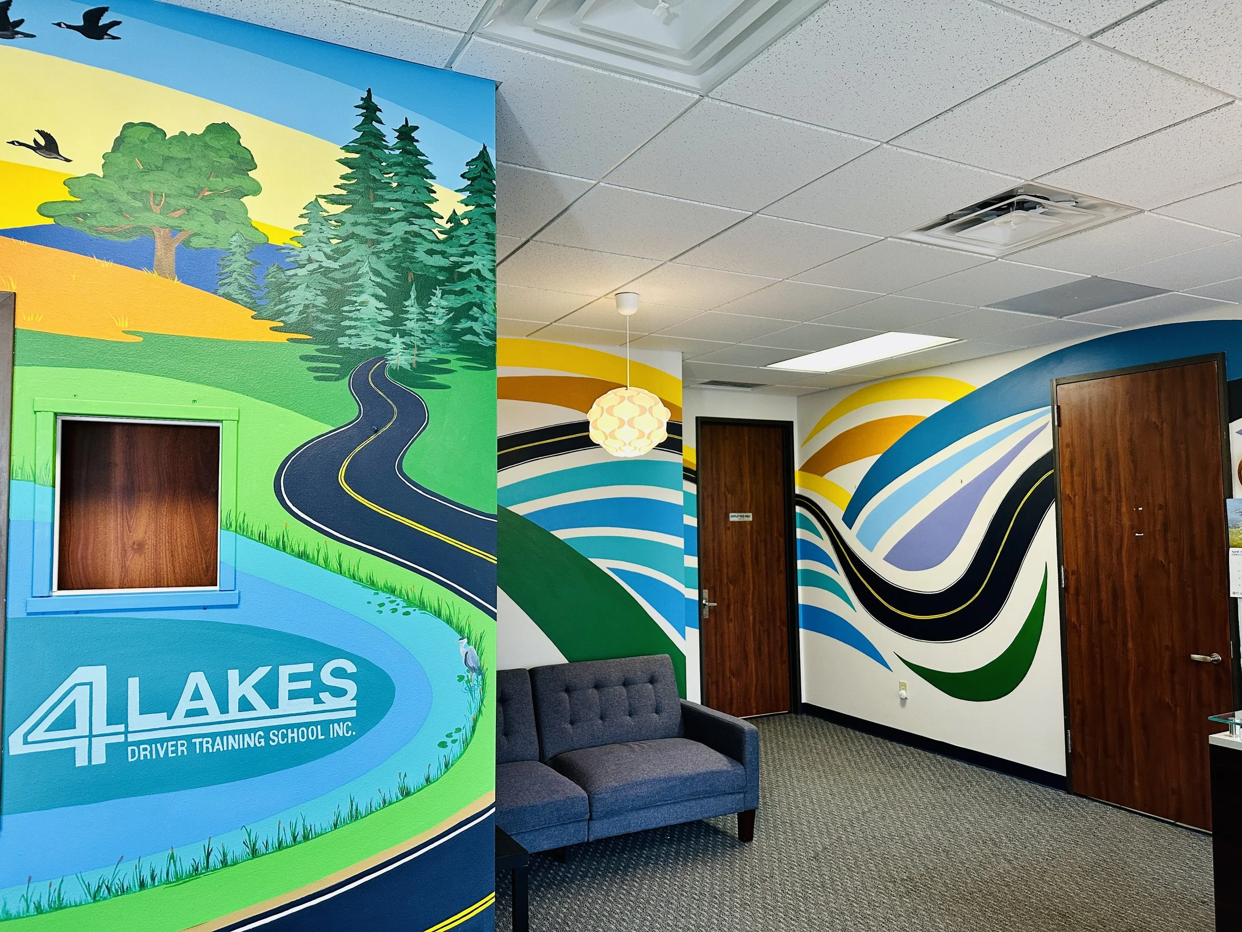 Interior of a driver's training school office with colorful mural walls depicting roads and nature, a small gray couch, and closed wooden doors.