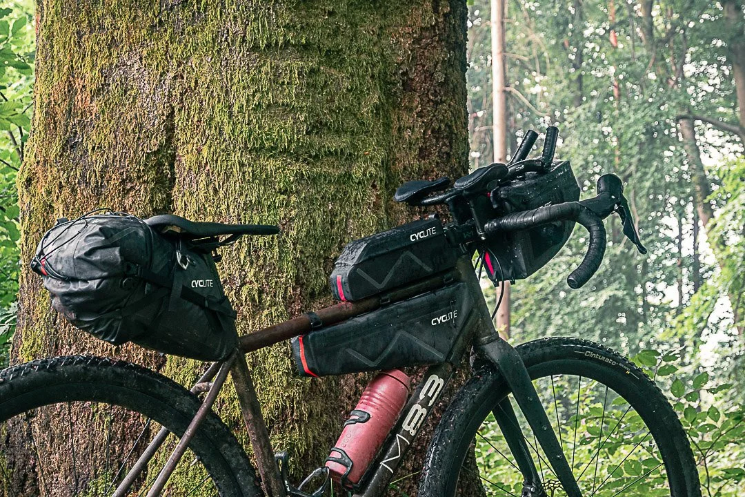 Ein Fahrrad mit Gepäcksäcken steht an einem Baum in einem Wald und ultraleichtem Gepäck. Packliste von Patrick Zasada