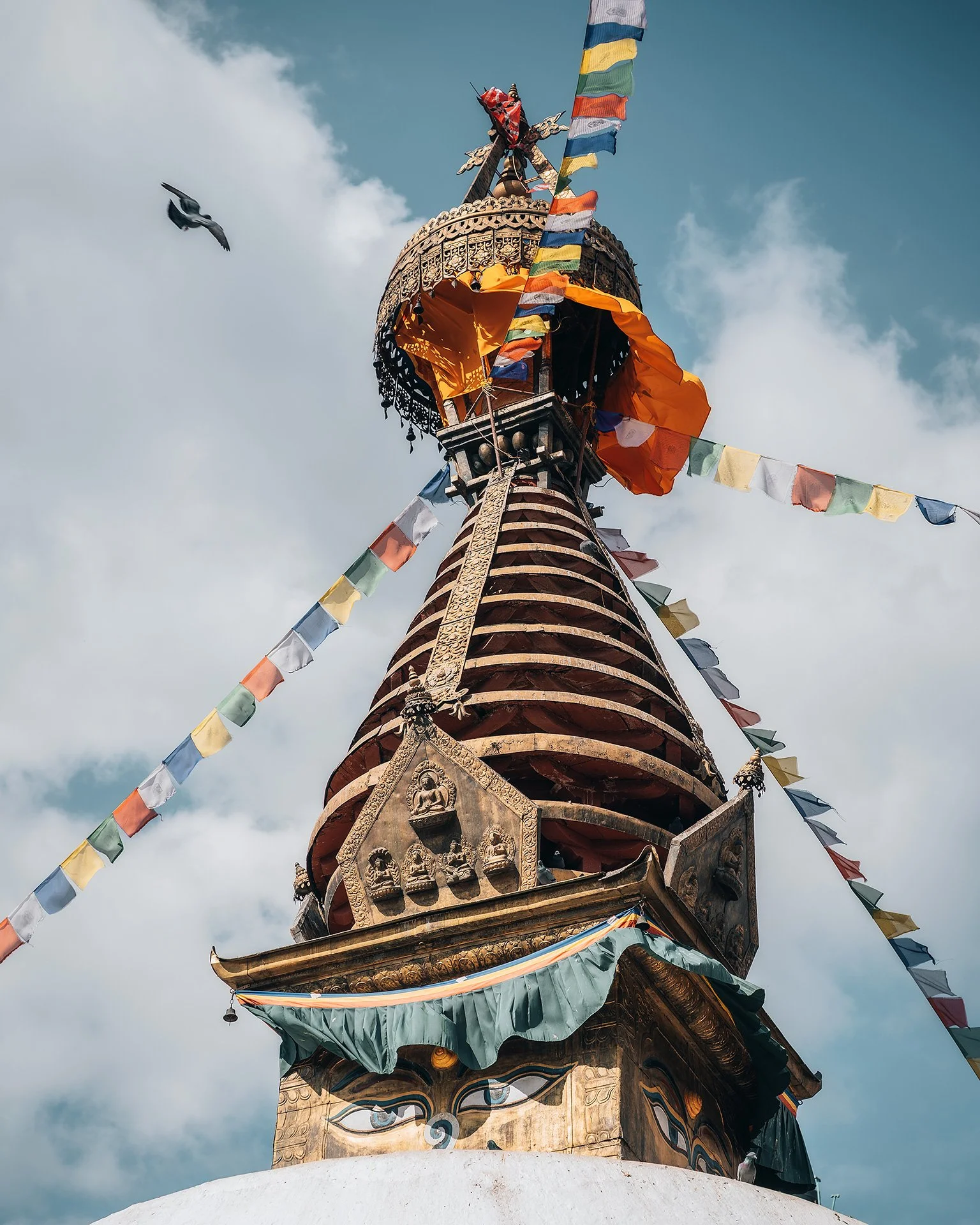 Una torre decorata con bandiere di preghiera colorate e ornamenti dorati, con un cielo nuvoloso sullo sfondo.