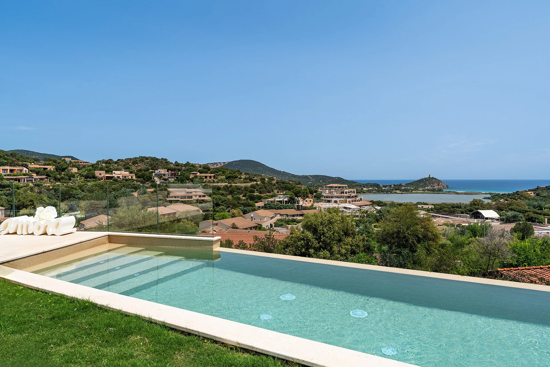 Vista panoramica di un paesaggio costiero con case e montagne, piscina e decorazioni in primo piano