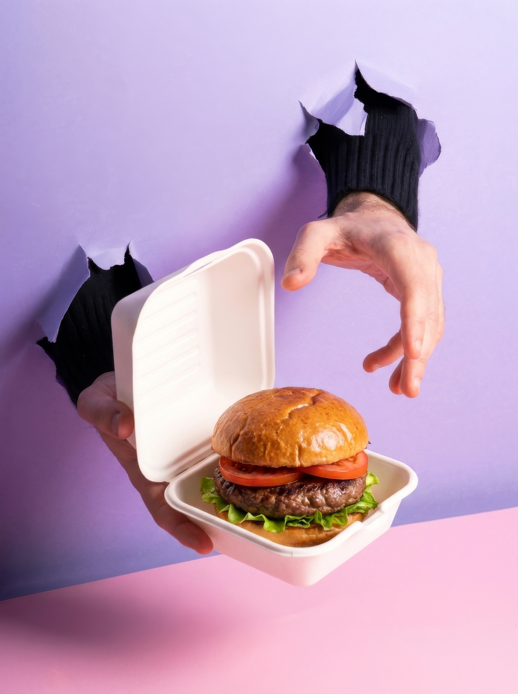 Una mano stringe una confezione di contenitore per hamburger con un hamburger dentro, con una mano che sembra uscire dal buco di cartone.