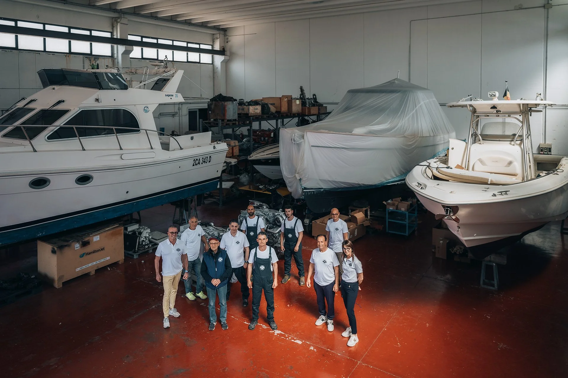 Gruppo di persone in piedi in un'officina con barche a motore e attrezzi.