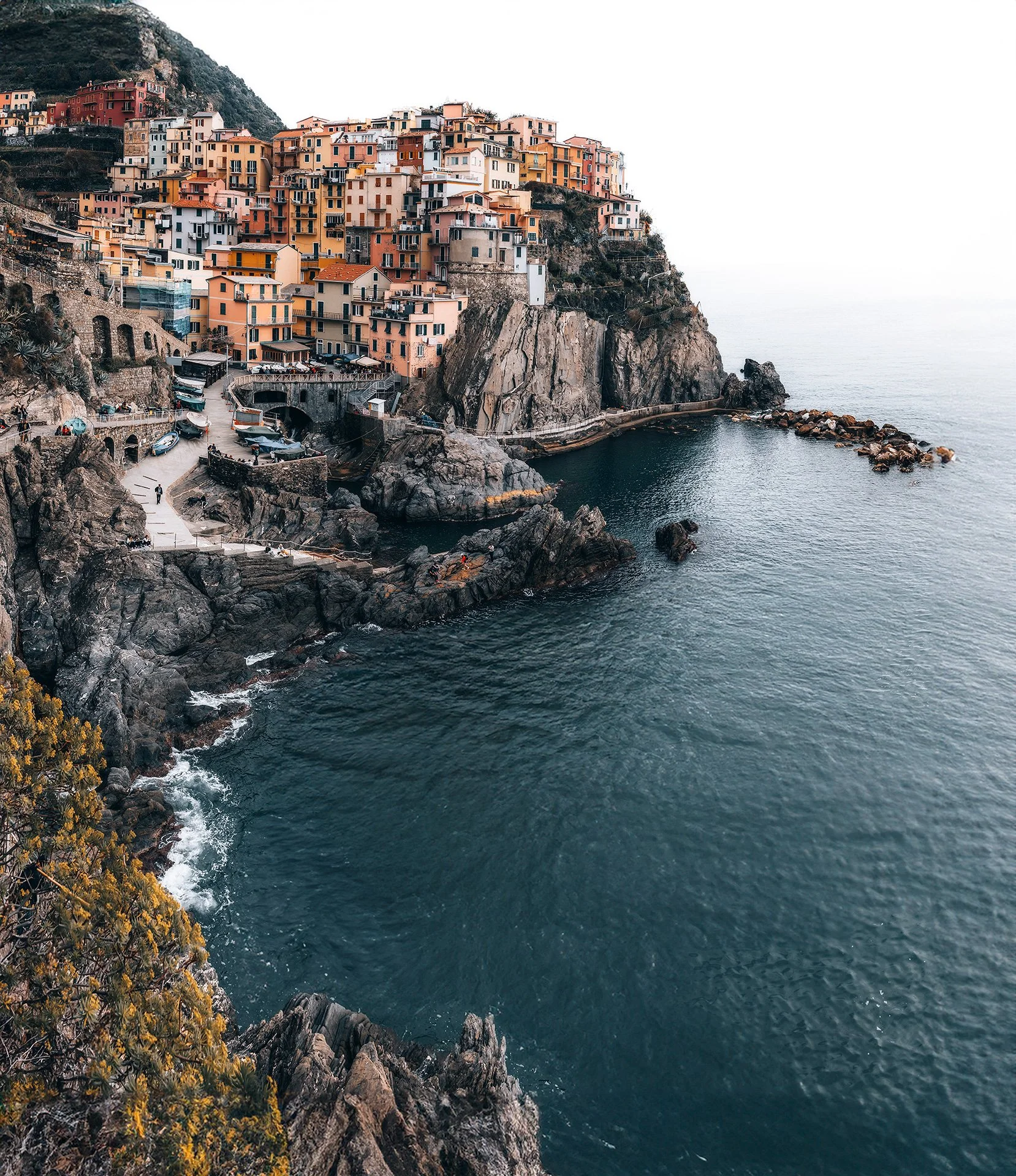 Casa colorata costruita su una scogliera a picco sul mare con un molo e alcune barche ancorate davanti.