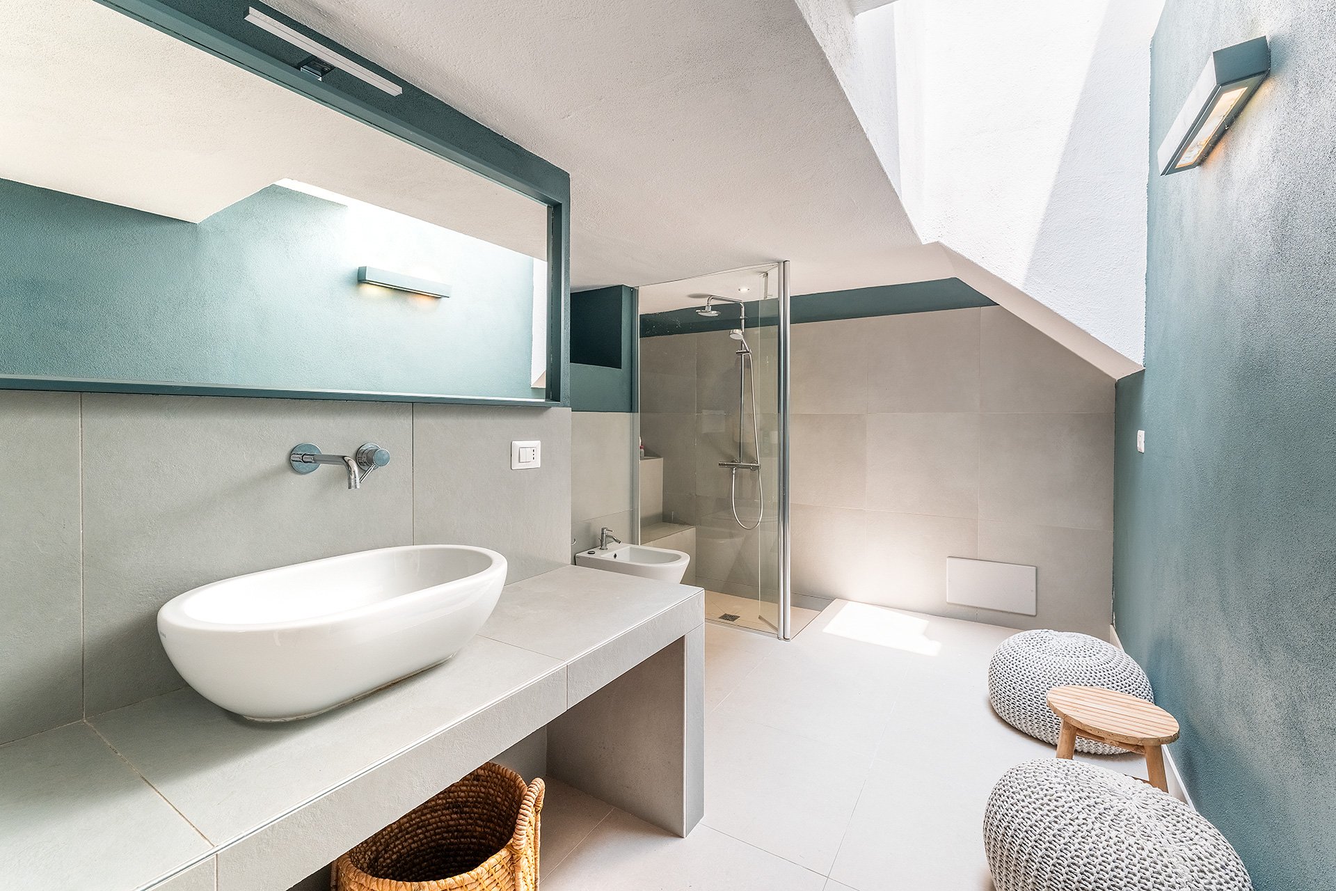 Bagno moderno con vasca, lavabo, bidet e cabina doccia, pareti azzurre e illuminate con luce naturale e lampada