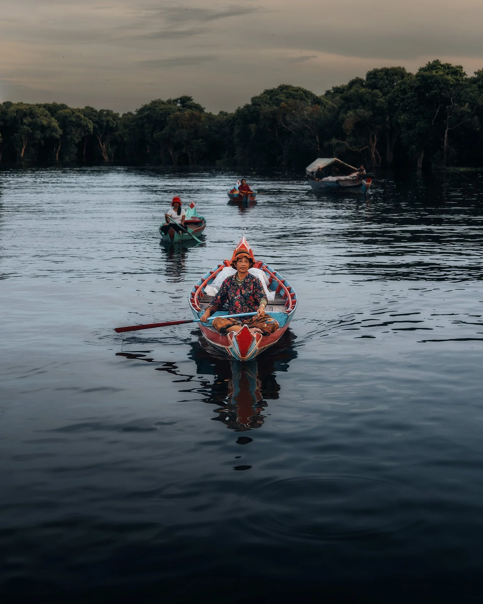 Una donna e altre persone in barche sul fiume, circondate da alberi, al tramonto.