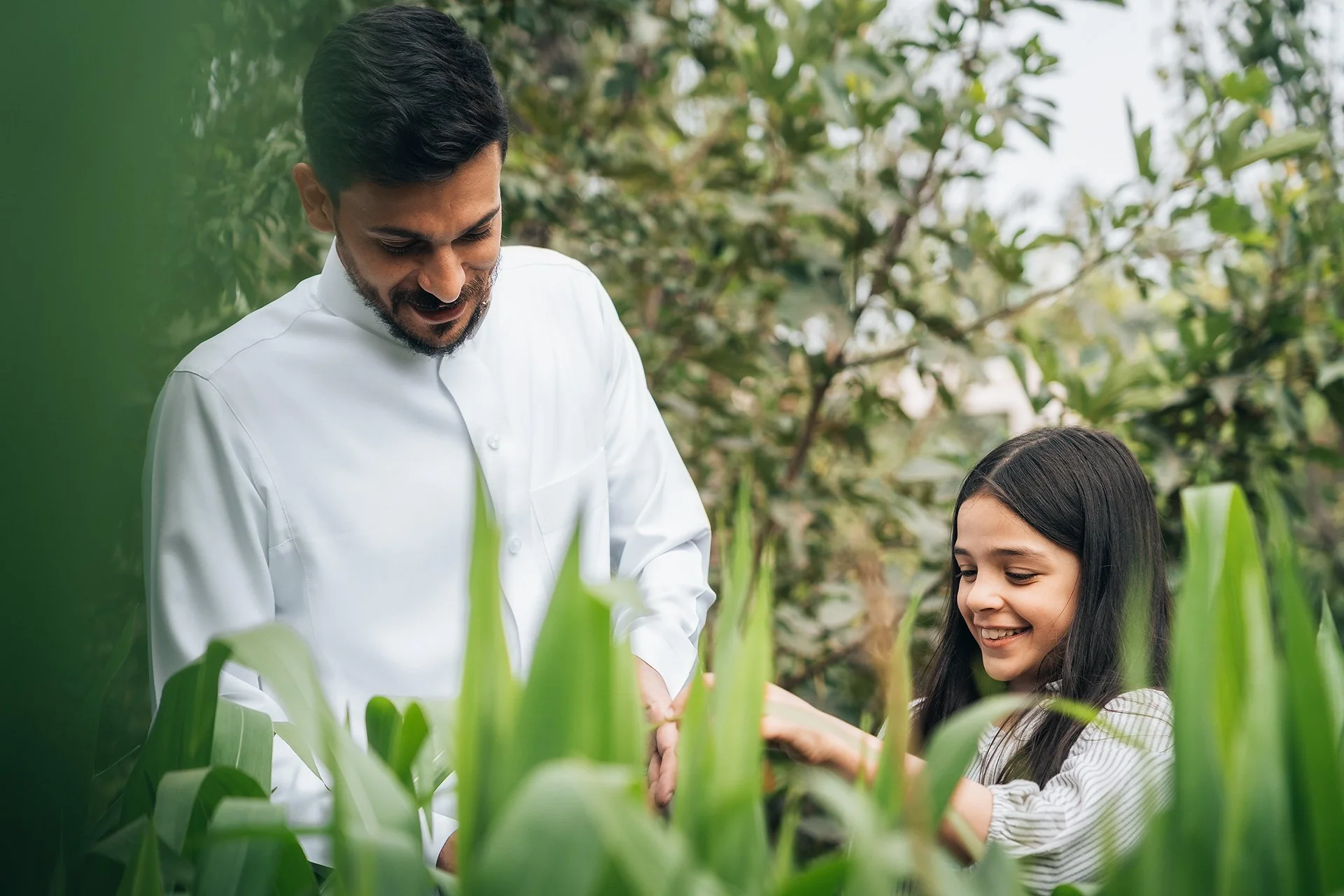 Un uomo e una ragazza sorridenti che lavorano insieme tra piante verdi in un ambiente all'aperto.