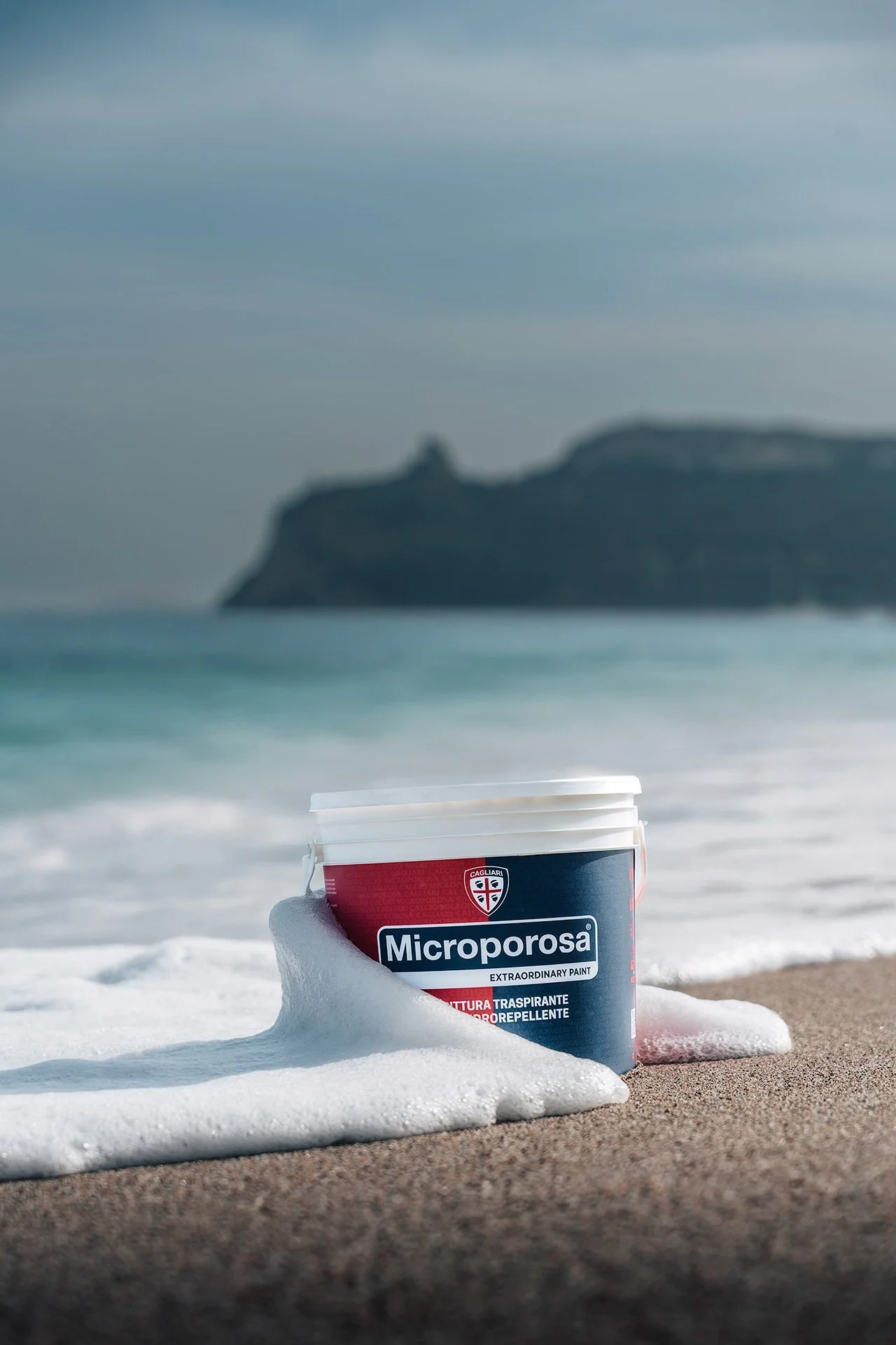 Barattolo di vernice Microporosa con schiuma sulla spiaggia con mare e scogliera sullo sfondo.