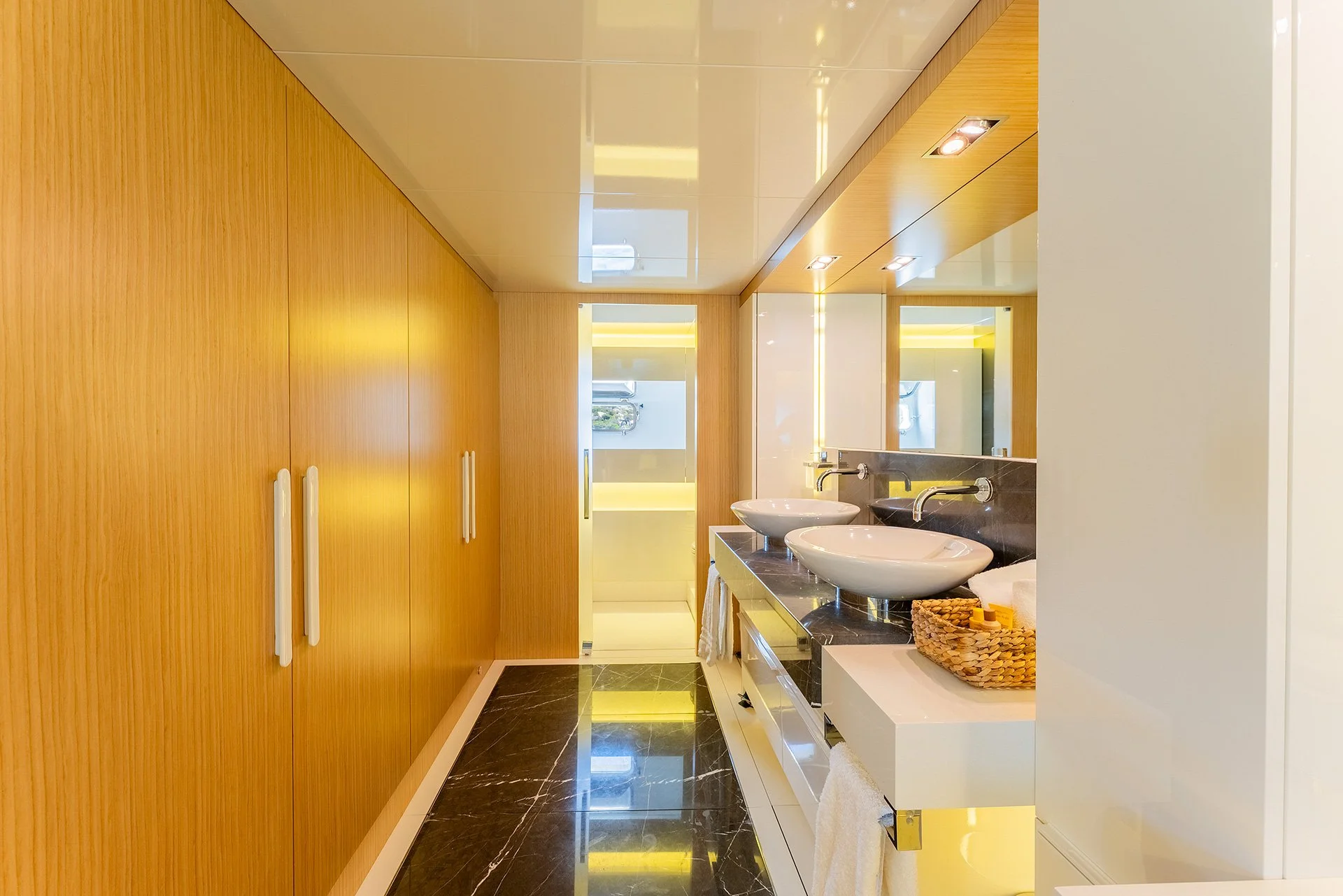 Bagno moderno con doppio lavabo, specchio grande, pareti di legno chiaro, pavimento in marmo nero lucido, asciugamani beige e cesta di vimini