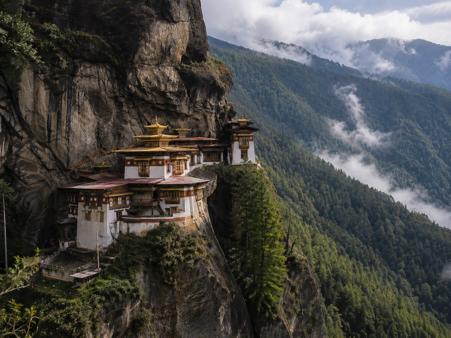 Monastero buddista appollaiato su una scogliera in montagna, circondato da foresta e nuvole.