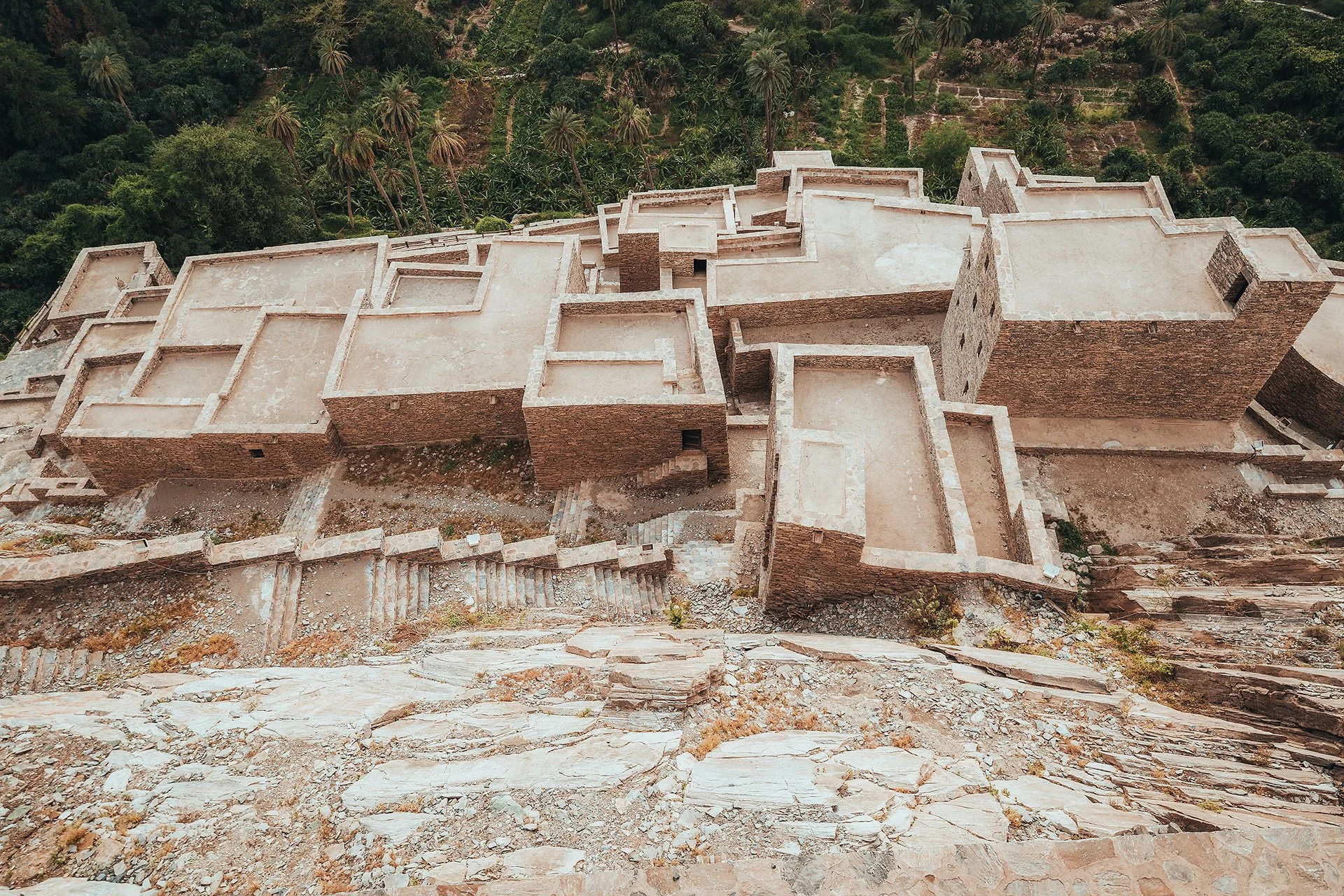 Rovine di un antico edificio in pietra con mura e terrazze, circondato da vegetazione e terreni collinari.