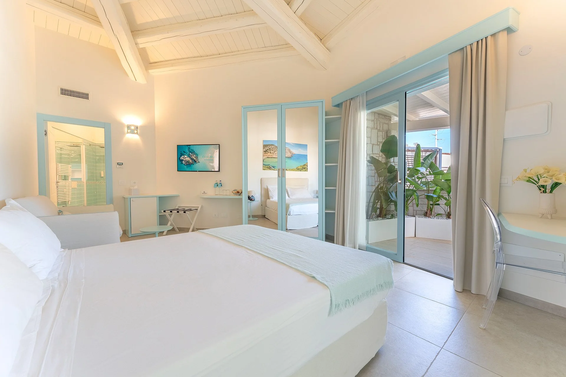Camera da letto con letto bianco, mobili color pastello, porta finestra con cortile e piante