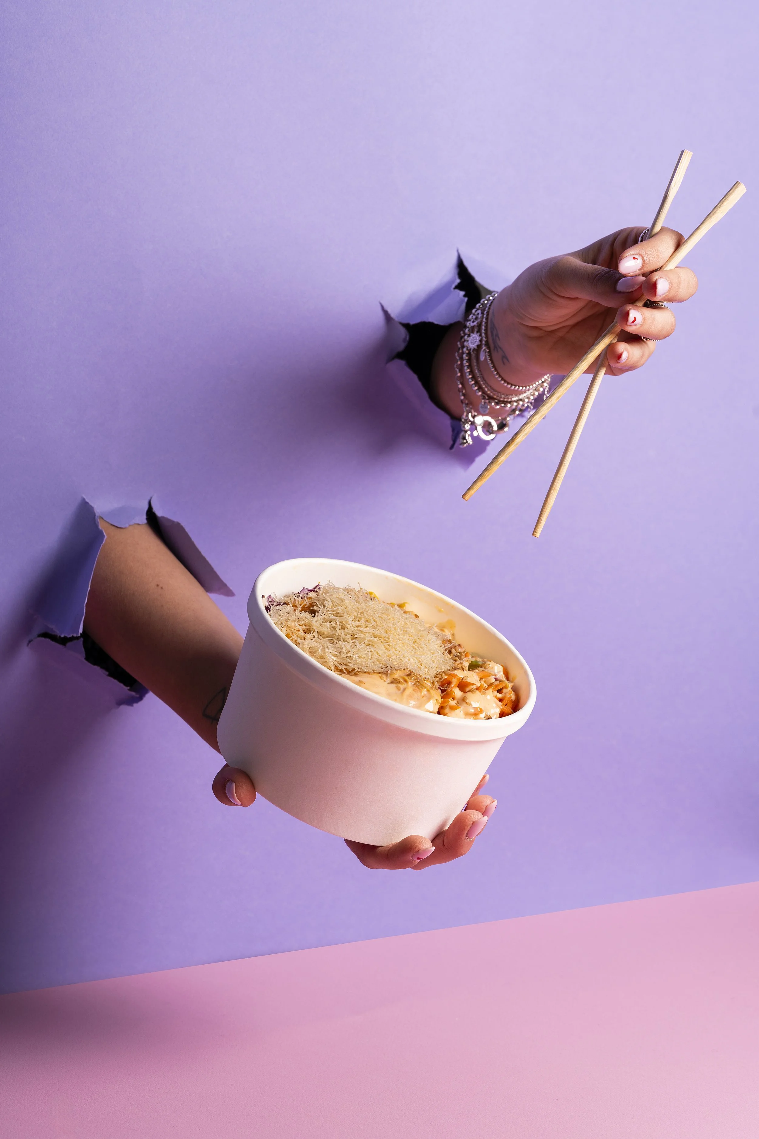 Una mano che spara una posizione di rivolta attraverso un buco nel muro, con una ciotola di cibo con formaggio grattugiato. sfondo sfumato viola e rosa.