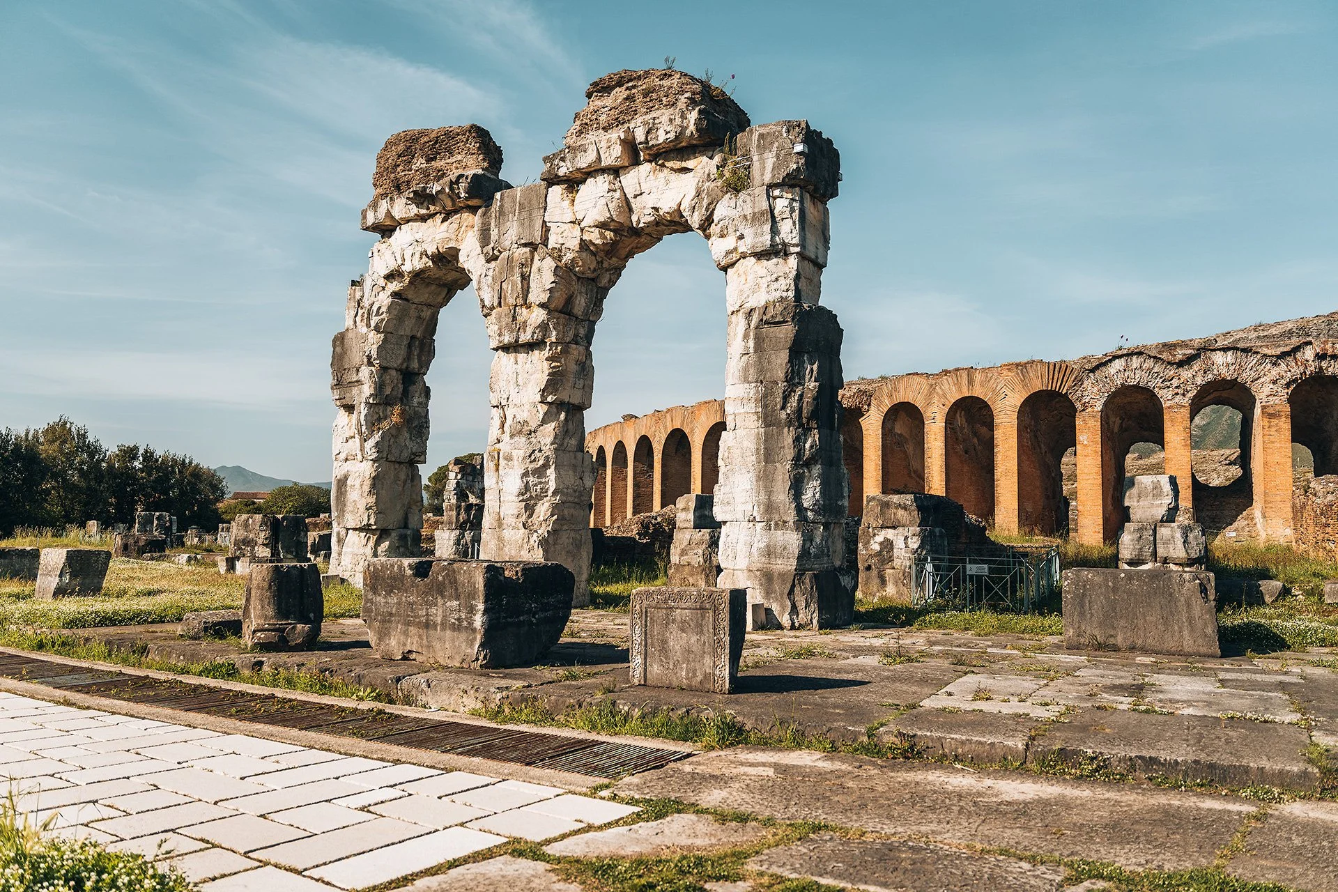 Resti di un antico teatro romano con archi in pietra, parte di strutture architettoniche antiche, con marmi e pietre visibili, sotto un cielo sereno.