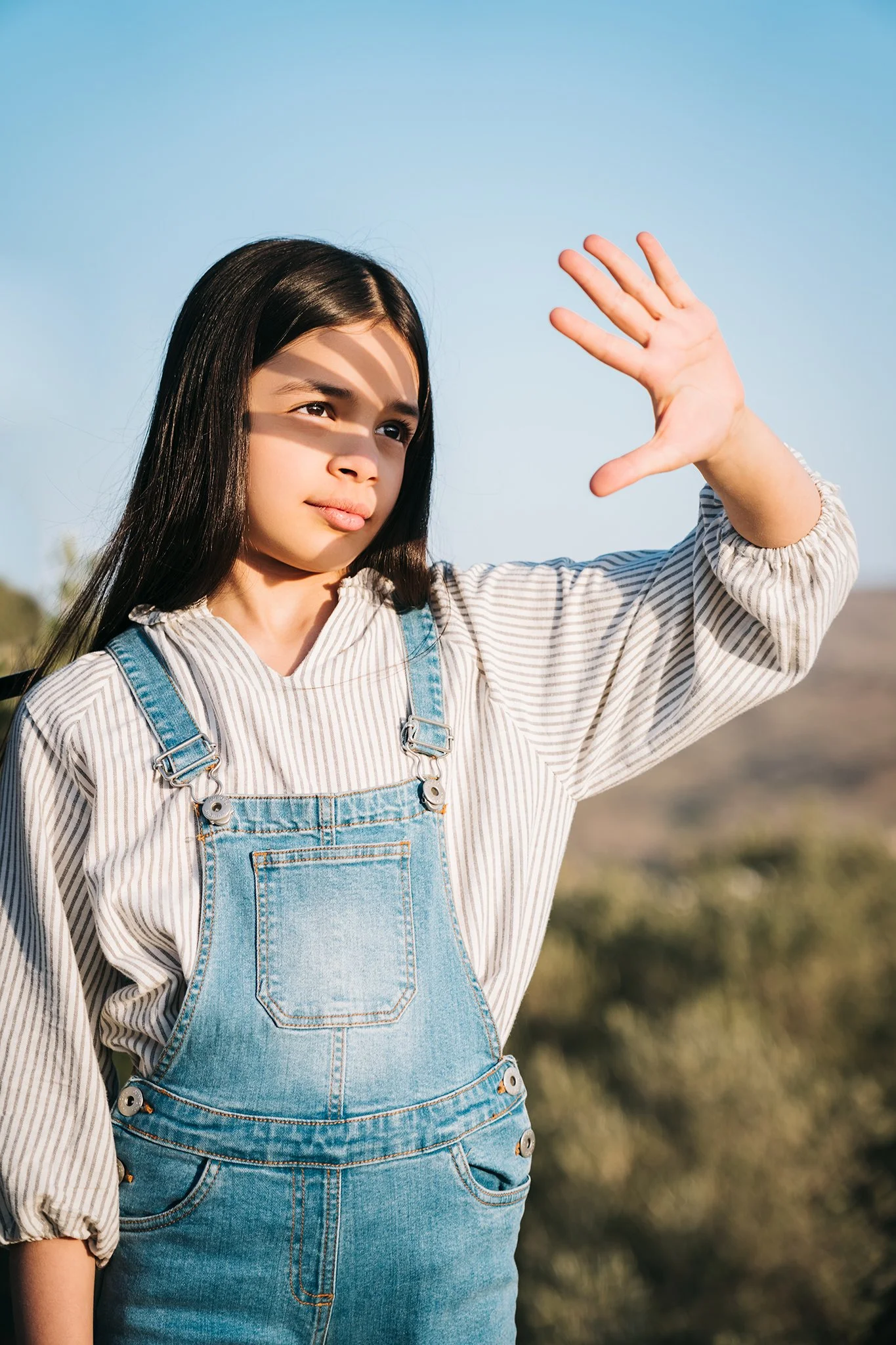 Ragazza giovane che alza una mano verso il cielo con uno sfondo di cielo azzurro e campagna