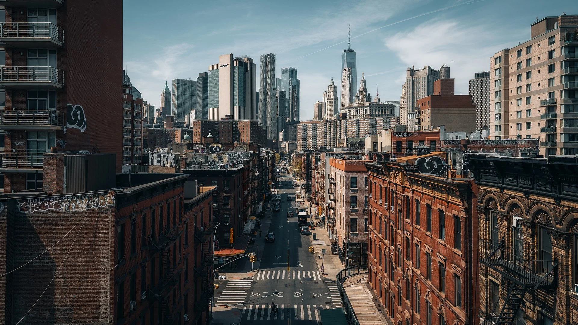 Veduta di una strada urbana a New York con grattacieli moderni sullo sfondo e edifici storici in primo piano, con graffiti sulle mura e un cielo sereno.