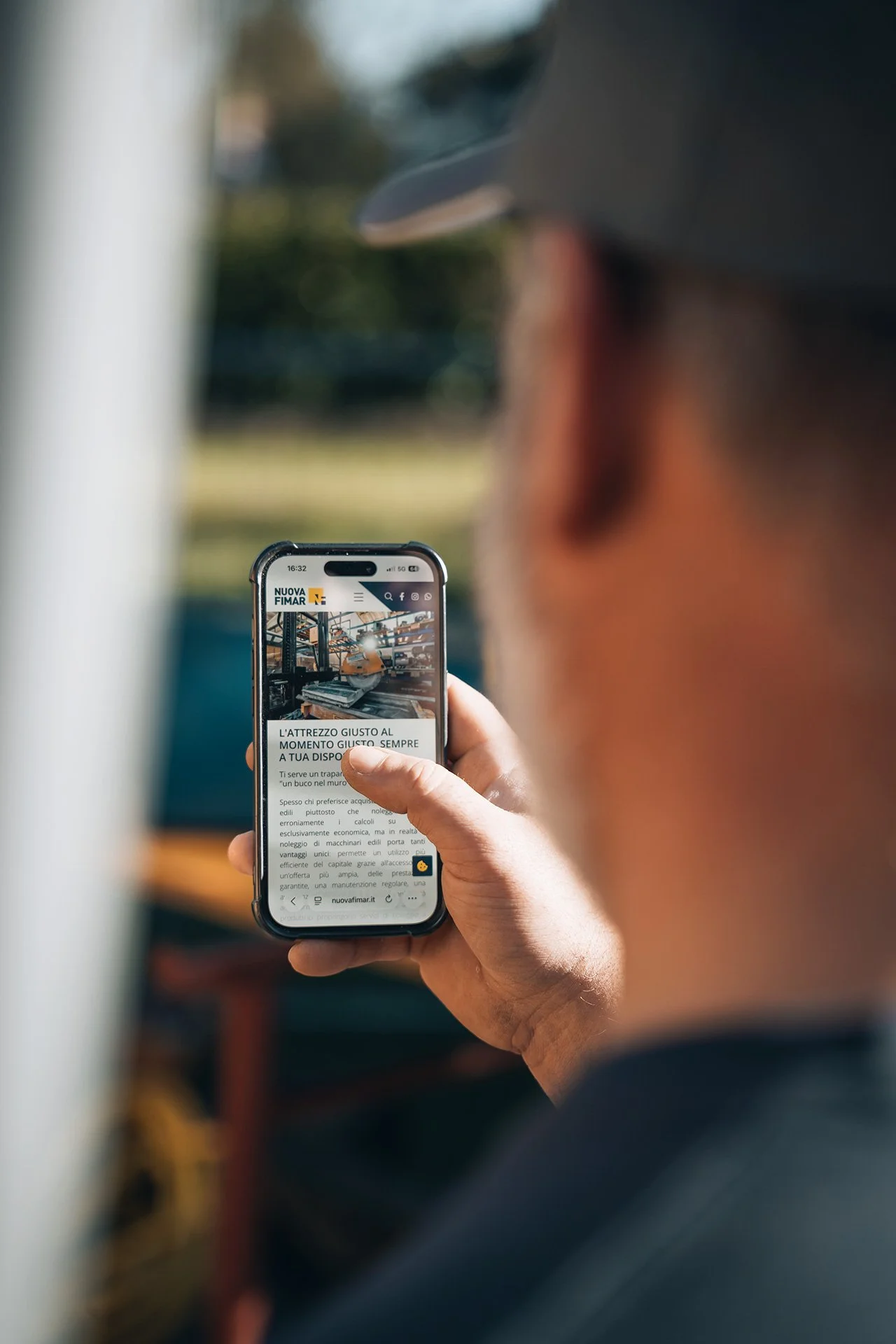 Persona che tiene in mano uno smartphone che mostra una pagina web di Nuova Fimar, con un'immagine di utensili ed edificio industriale sullo schermo.