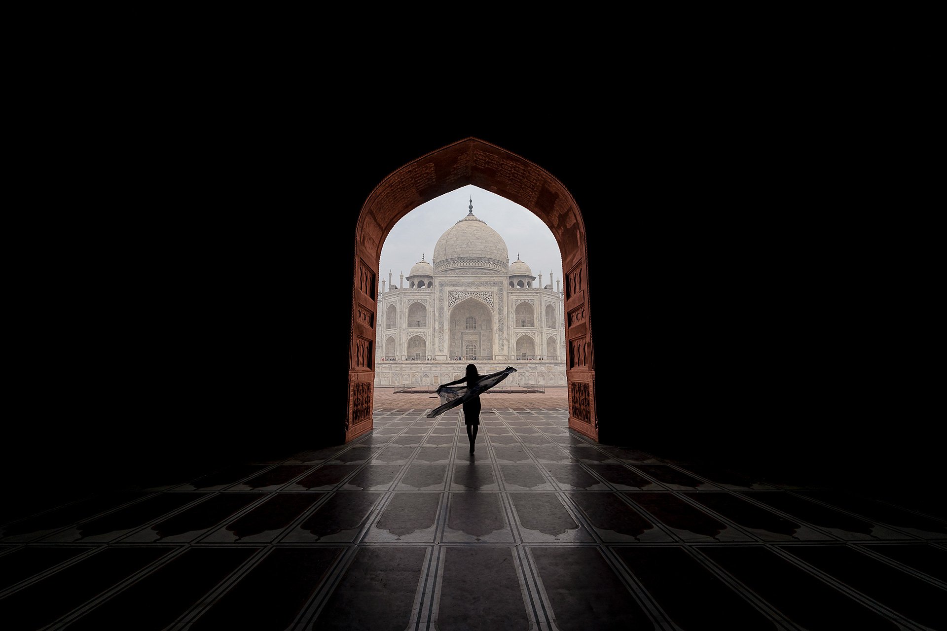 Vista del Taj Mahal visto da una porta aperta, con una bambina che corre con le braccia aperte