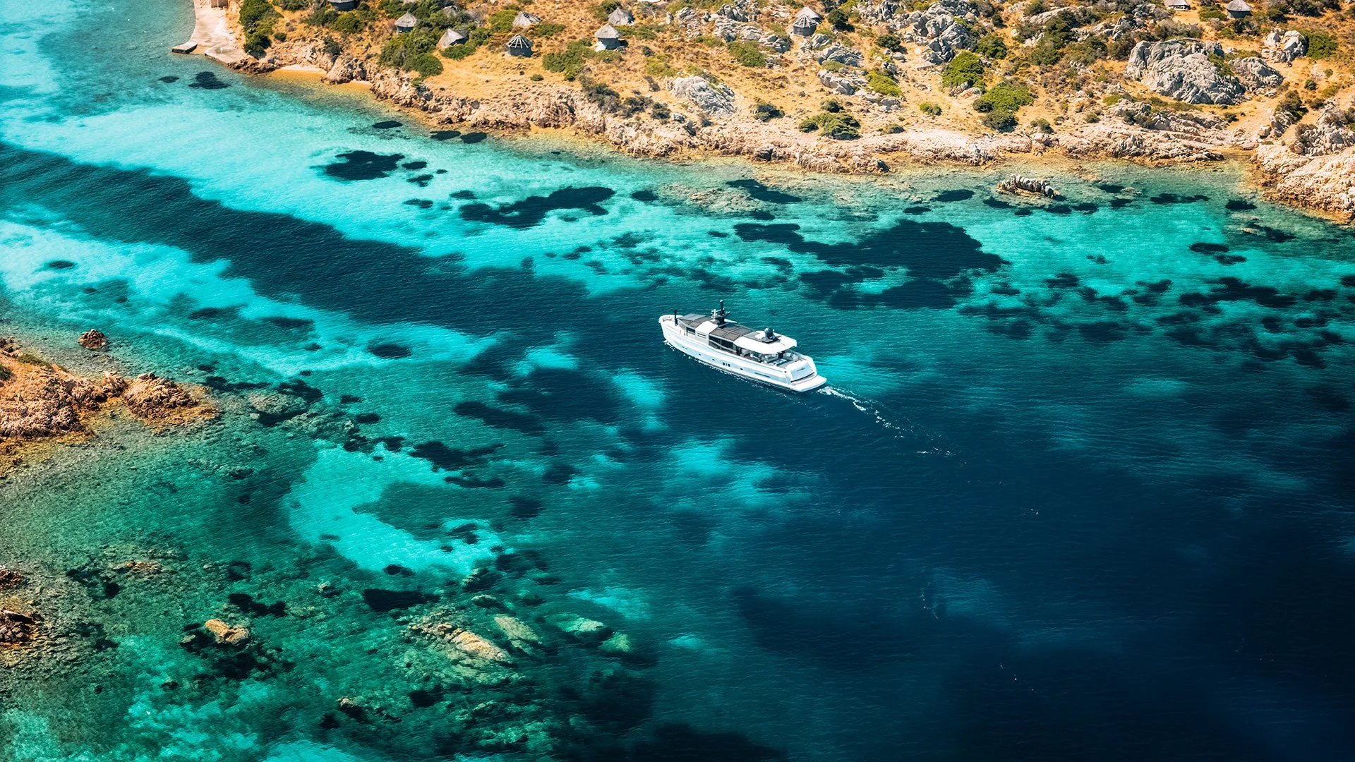Barca bianca che naviga in acque turchesi tra scogli e costa rocciosa con vegetazione.