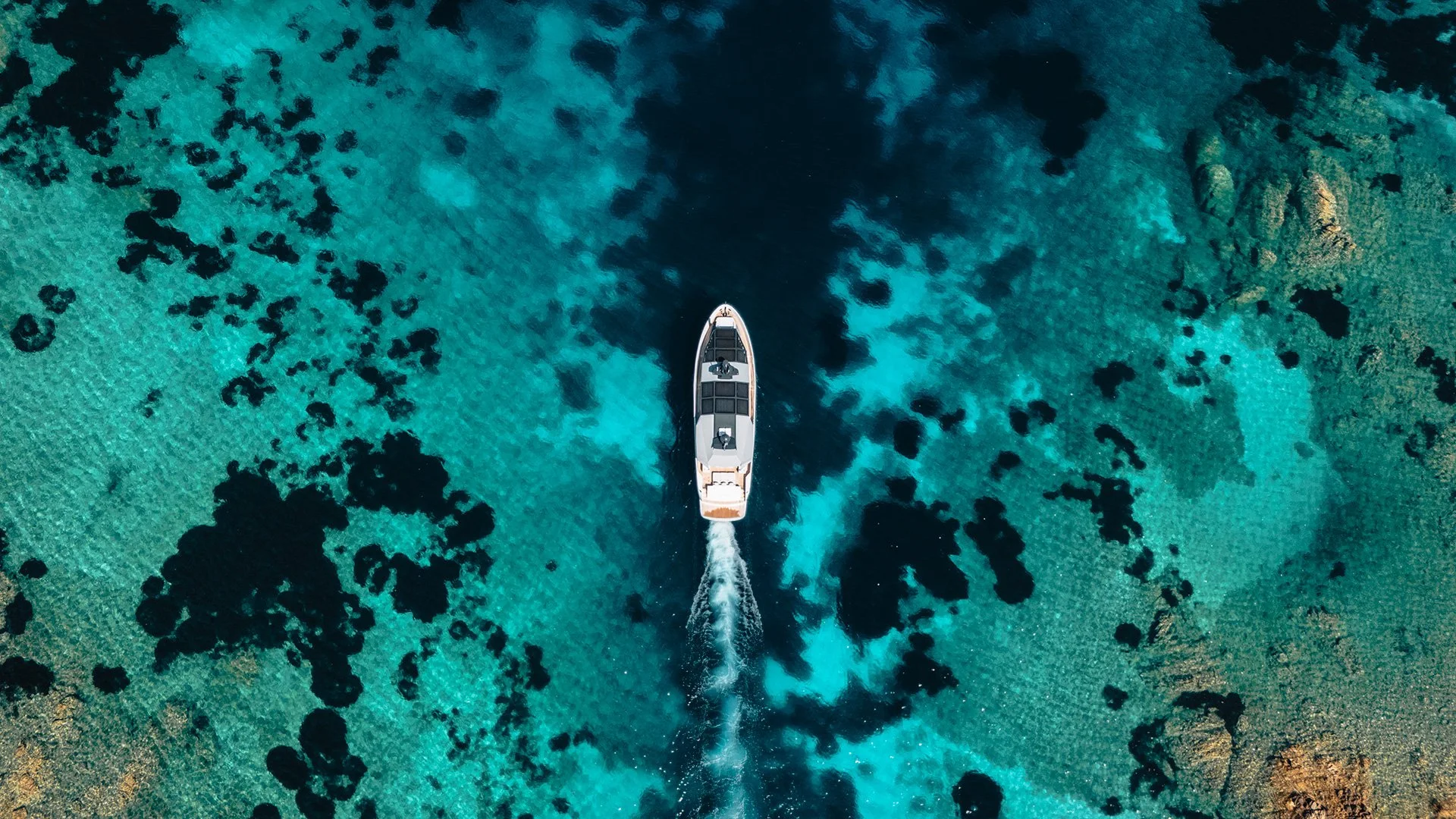 Immagine aerea di una barca in mare chiaro con formazioni di scogli e barriere coralline sotto l'acqua.