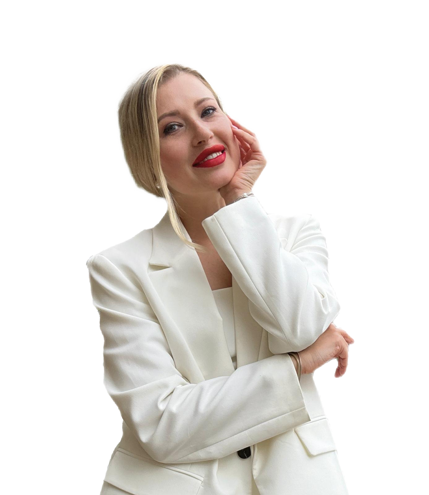 A woman with blonde hair and red lipstick, wearing a white suit, touching her face with one hand and crossing her arms.