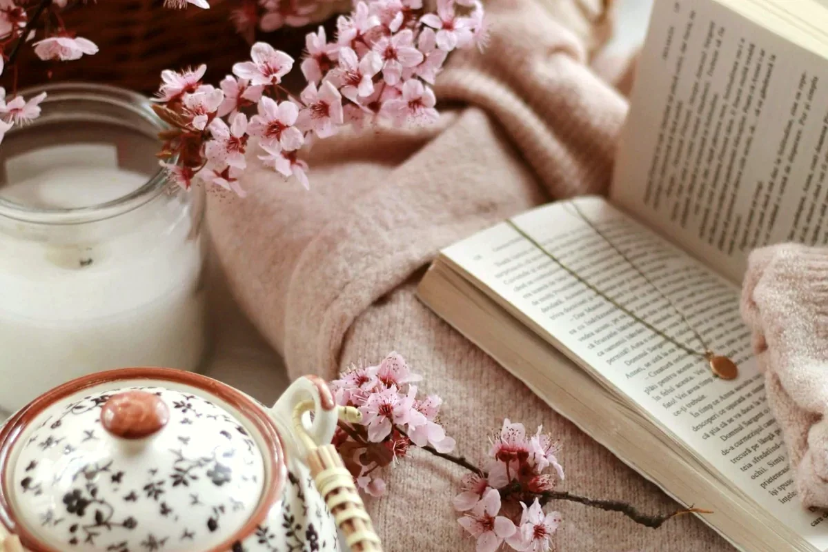 Cozy flatlay of an open book, teapot, and cup of tea on a table, representing a mindful screen-free bedtime ritual.