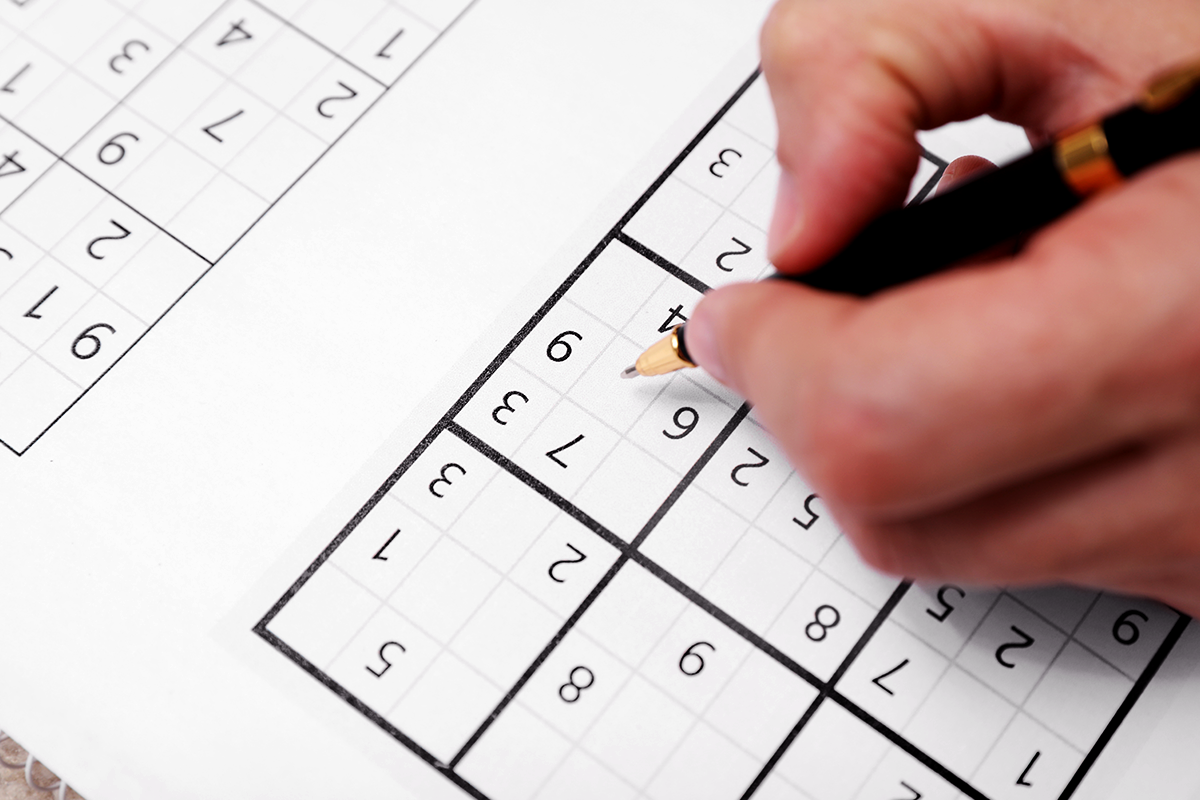Hand solving a Sudoku puzzle with a black pen on a printed puzzle page