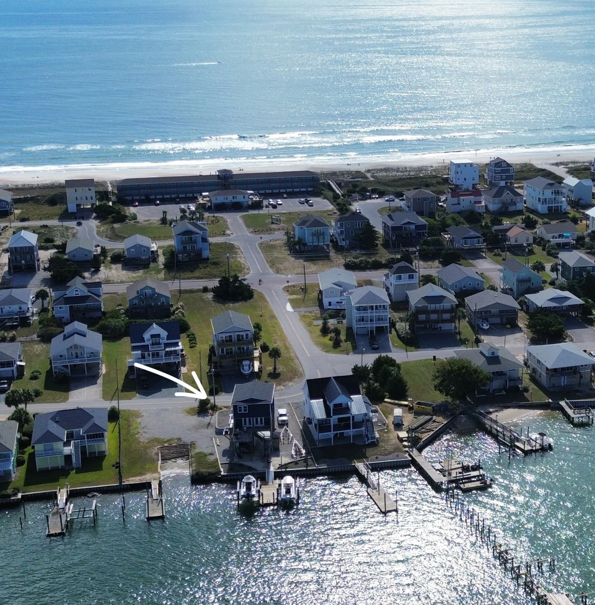 Aerial view of a beachside neighborhood with houses, docks, and the ocean in the background.