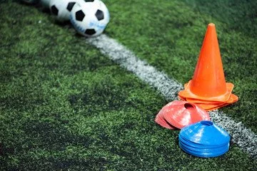 A soccer ball near an out-of-bounds line on a grassy field, with training cones and agility discs nearby.