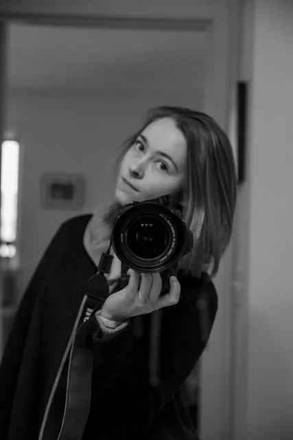 Woman taking a mirror selfie with a camera, in black and white.