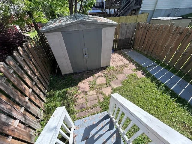 Backyard with wooden fence, lawn, paved pathway, small shed, and white porch stairs.