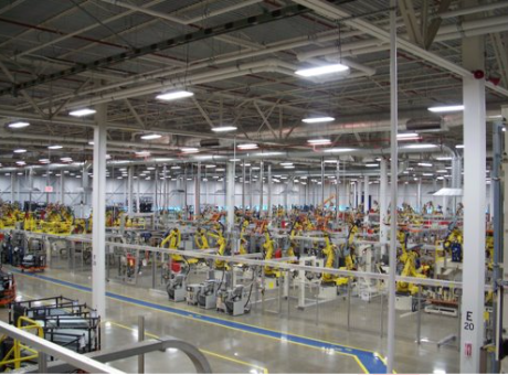 Factory assembly line with multiple yellow robotic arms working on machinery and components.