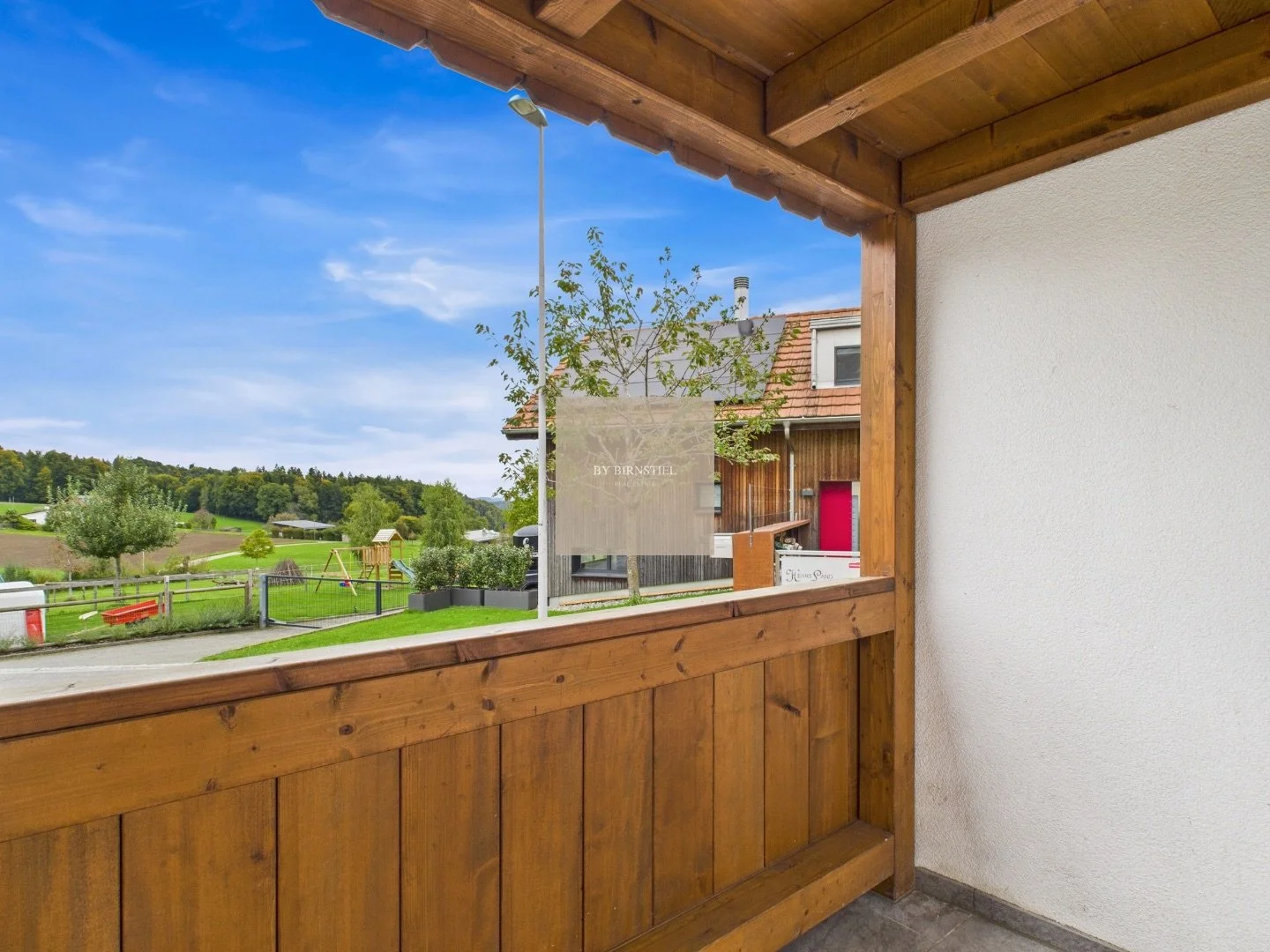 Überdachter Balkon mit Holzverkleidung und Blick in die ländliche Umgebung.