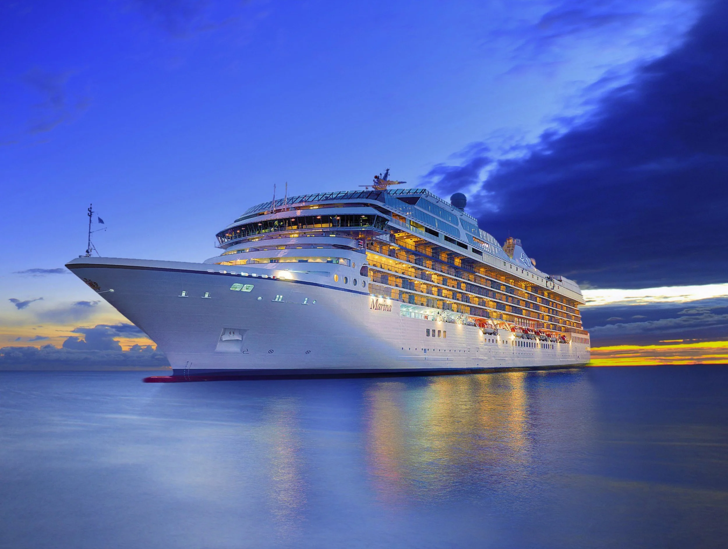 An Oceania cruise ship sailing on calm water during sunset, with a partly cloudy sky.