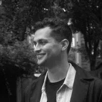 Black and white photo of a smiling man outdoors with trees in the background.